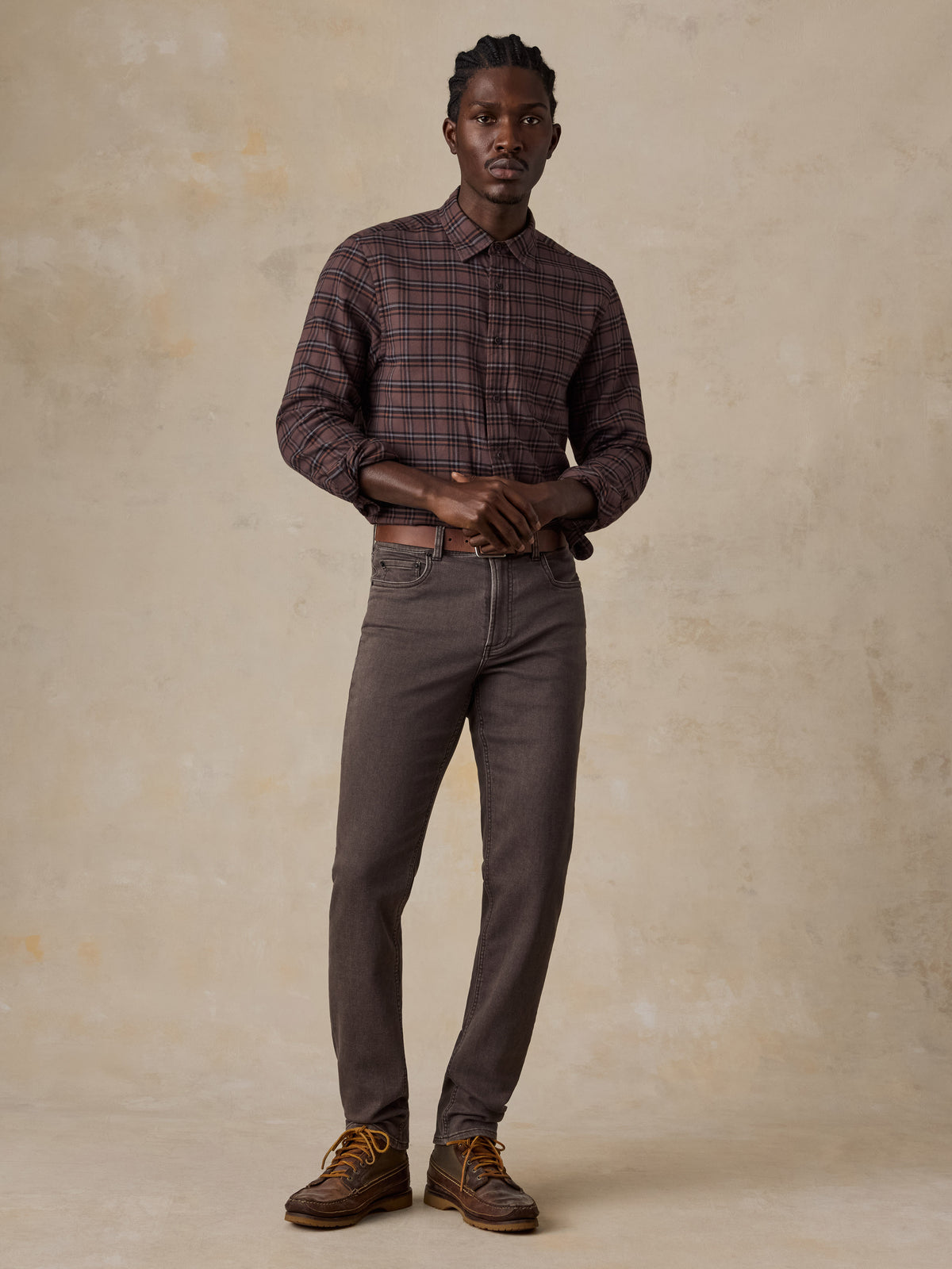 A man wearing a red plaid shirt, brown pants, and leather boots, image 5 of 5