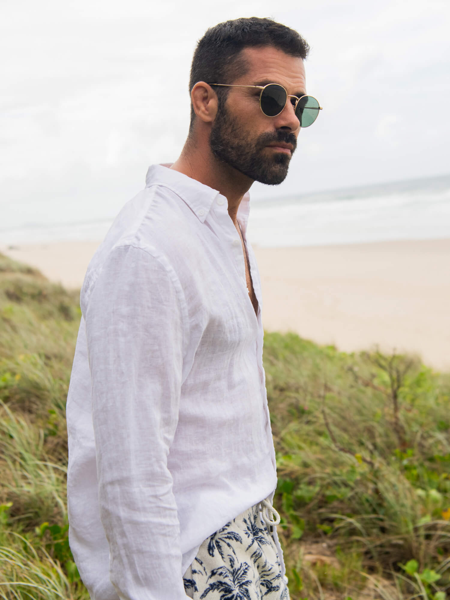 Man wearing a white linen shirt with palm tree printed shorts at the beach