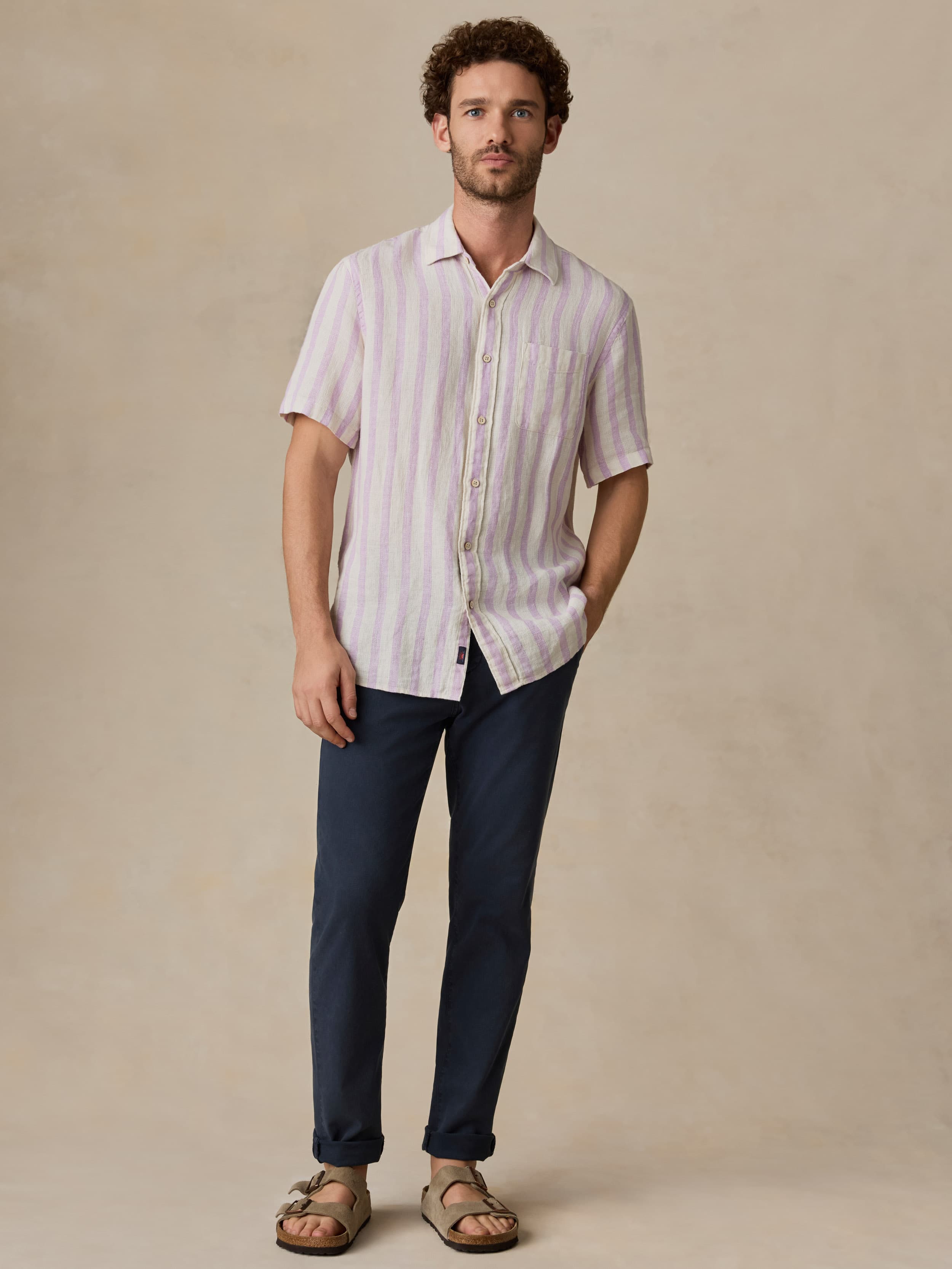 Man wearing a purple and white striped shirt and dark pants against a beige background