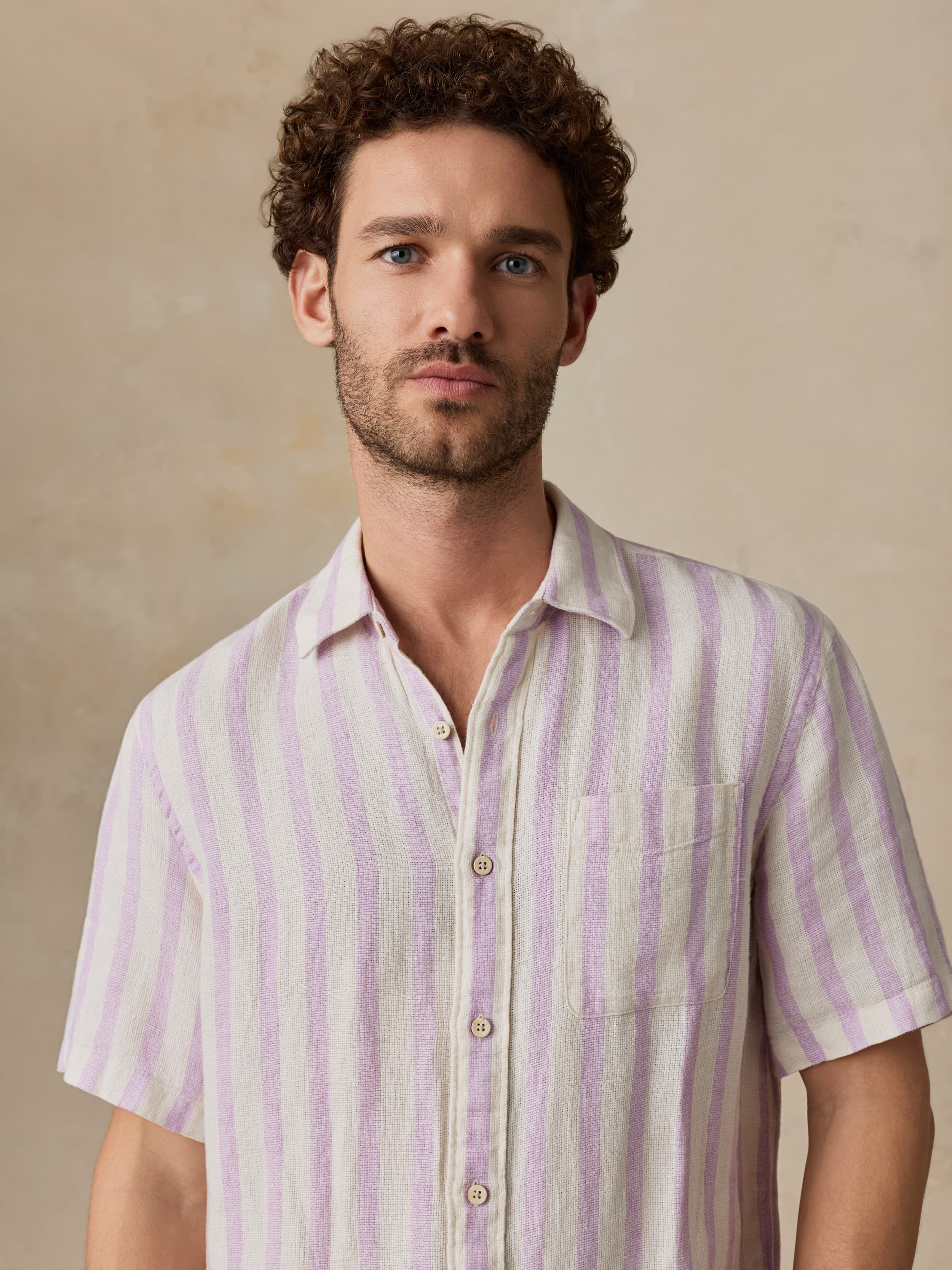 Man wearing a light purple and white striped shirt against a beige background