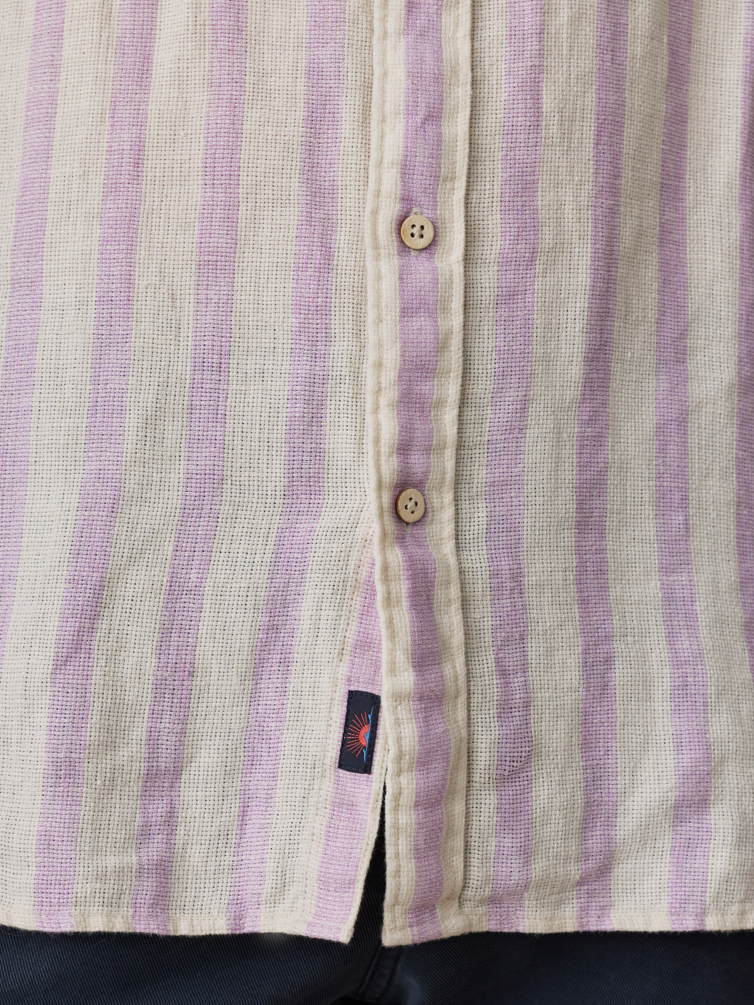 Close-up of a buttoned shirt with purple and white stripes and a Faherty brand label near the hem