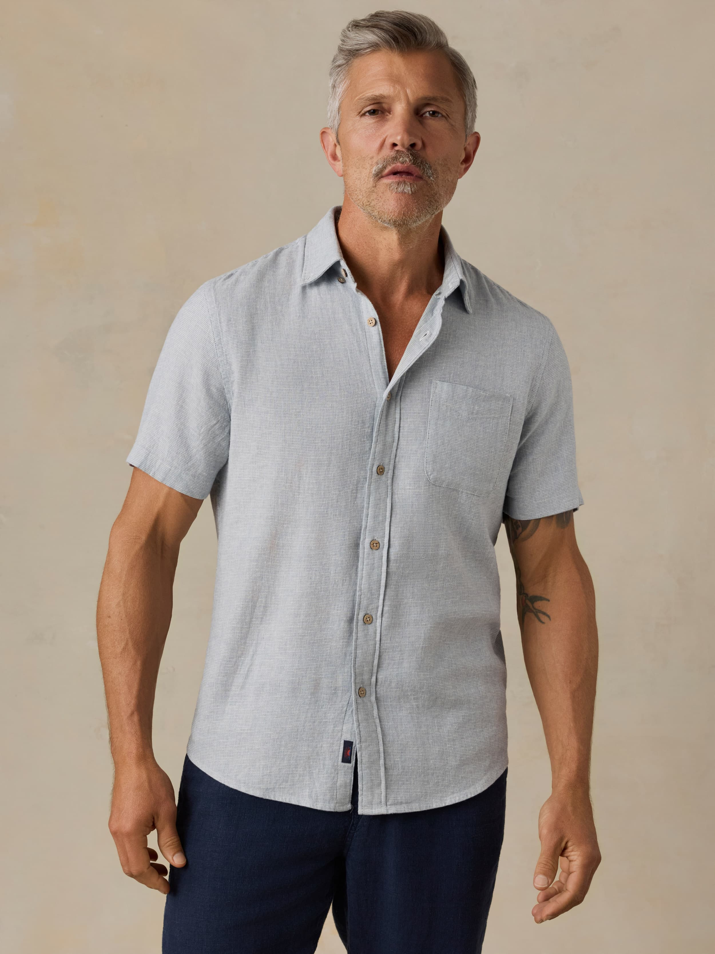 Man wearing a light blue short-sleeve shirt and dark blue pants against a beige background