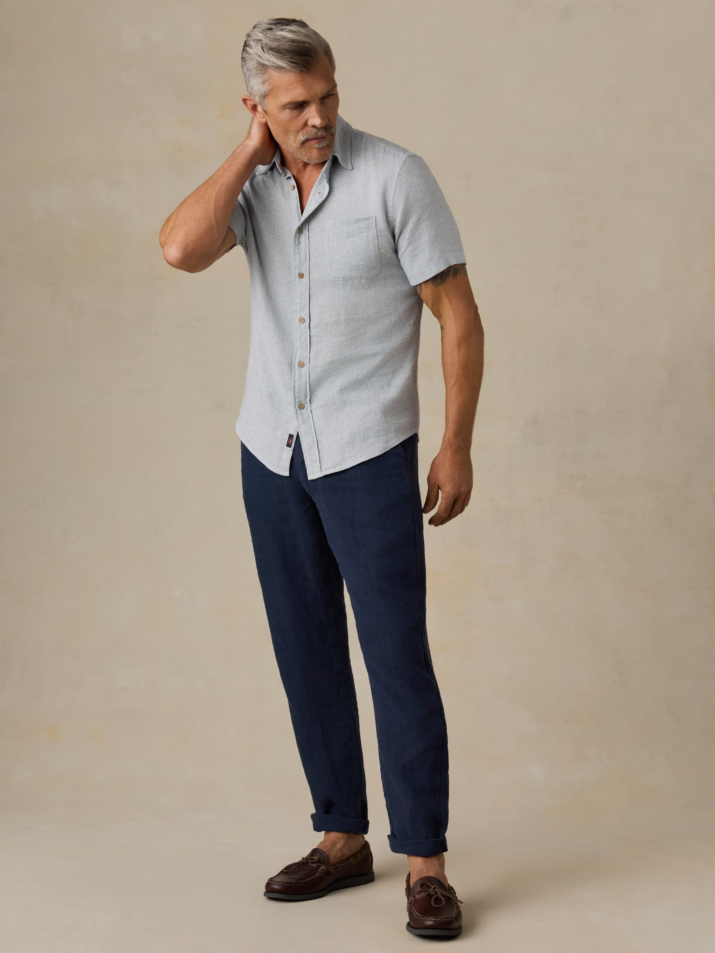 Man wearing a light blue short-sleeve shirt and dark blue pants against a beige background