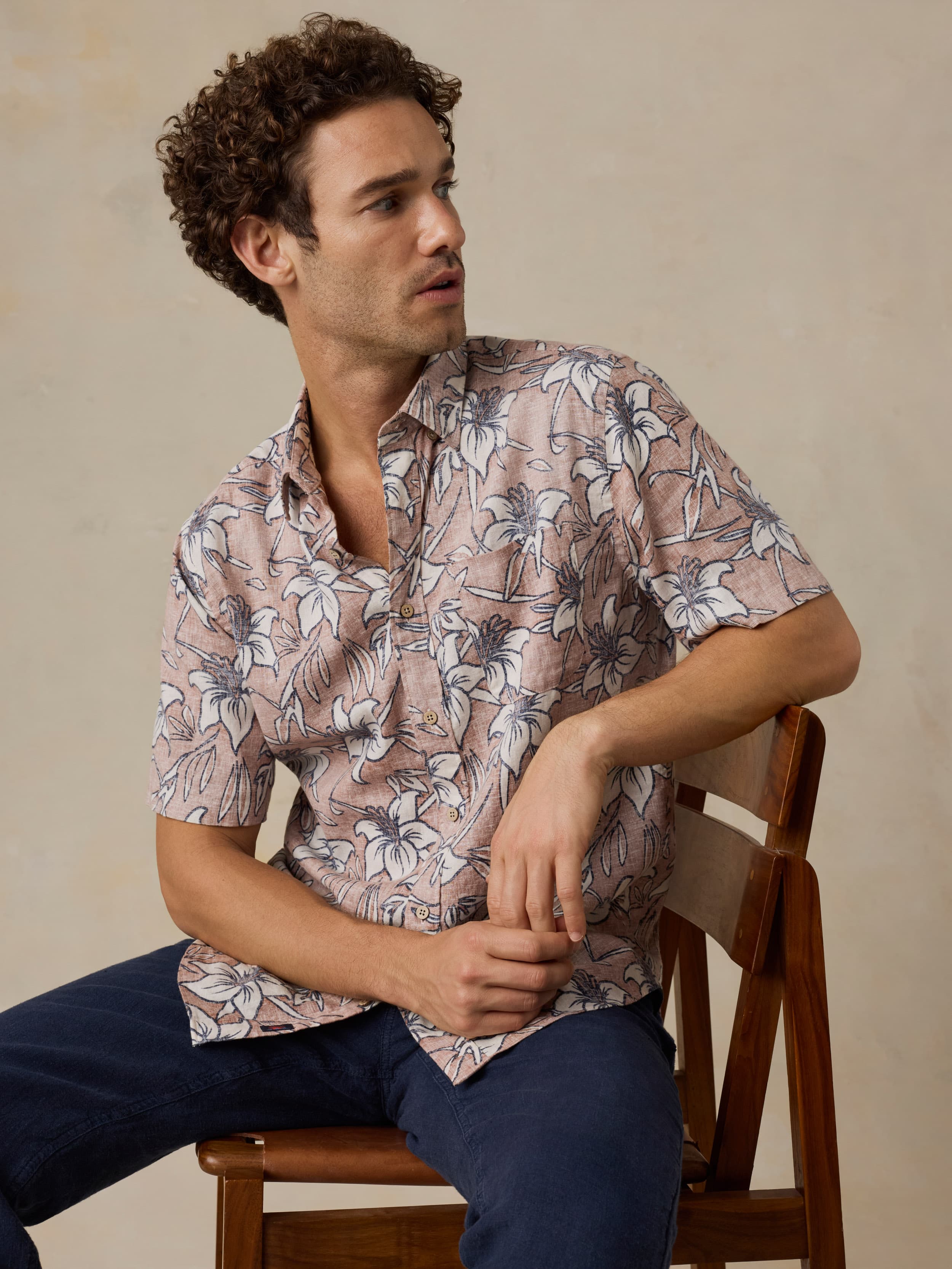 Man sitting on a wooden chair wearing a floral patterned shirt against a beige background