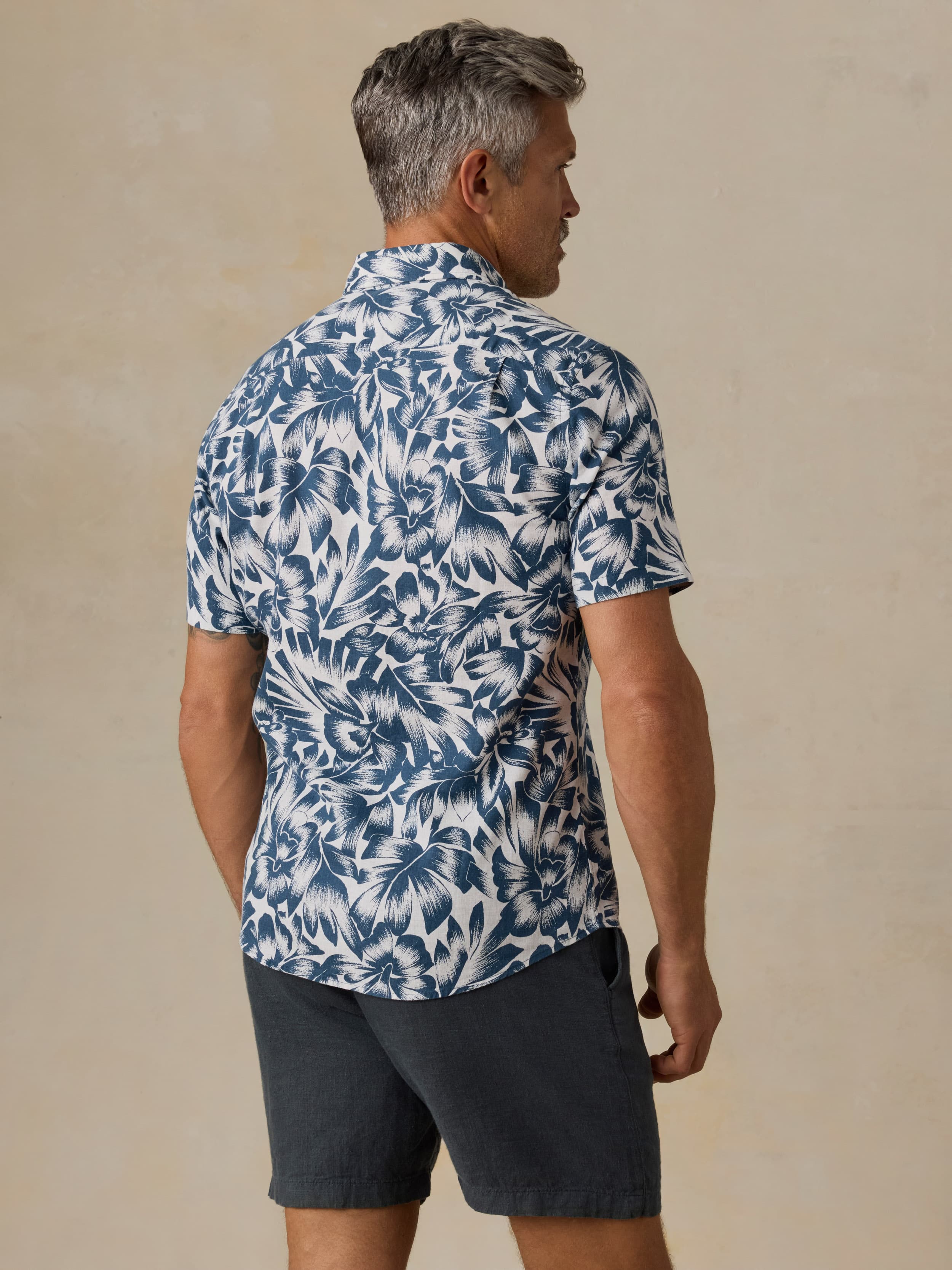 Man wearing a blue and white patterned shirt with navy shorts against a beige background