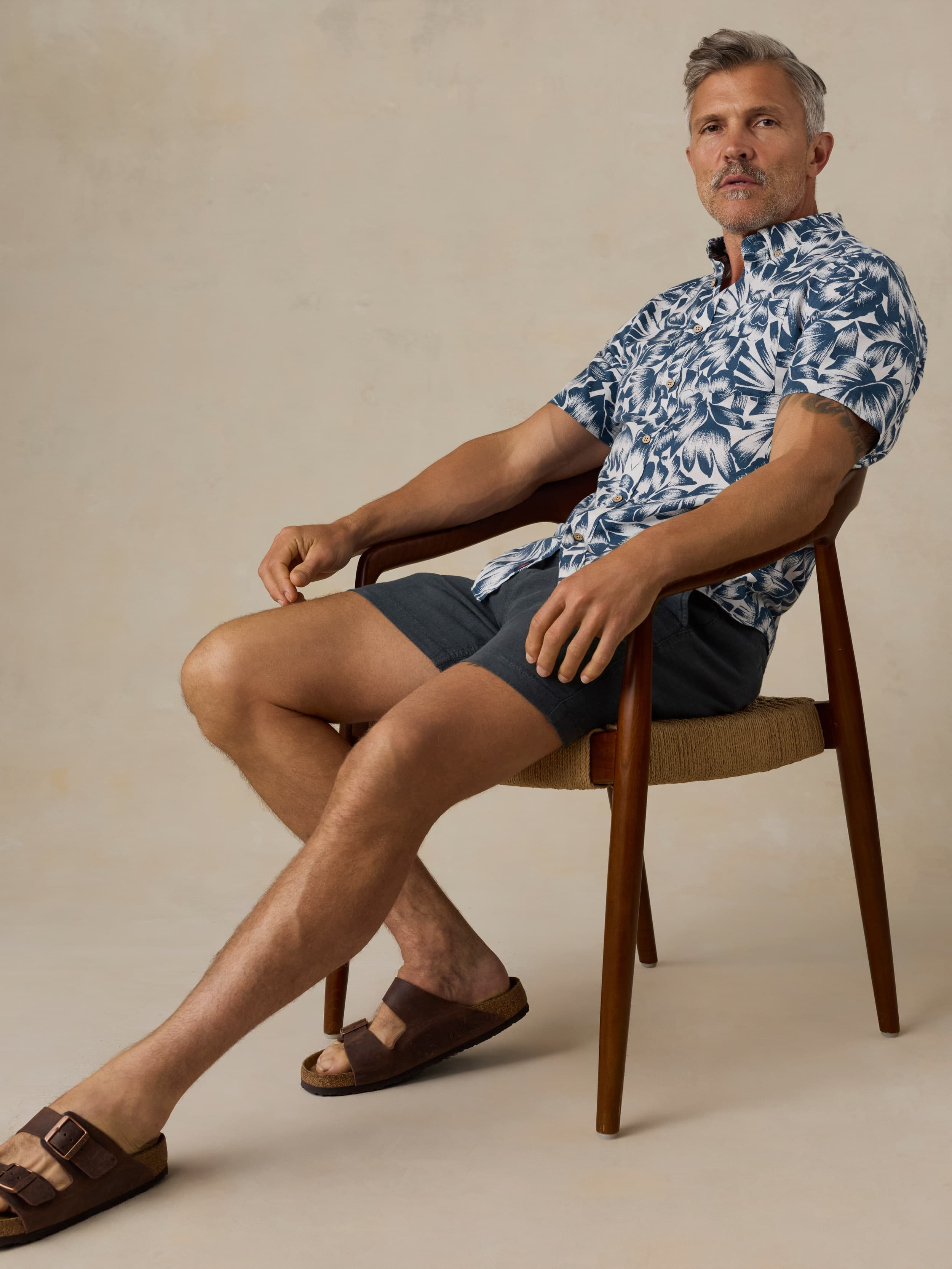 Man wearing a blue and white patterned shirt with navy shorts against a beige background