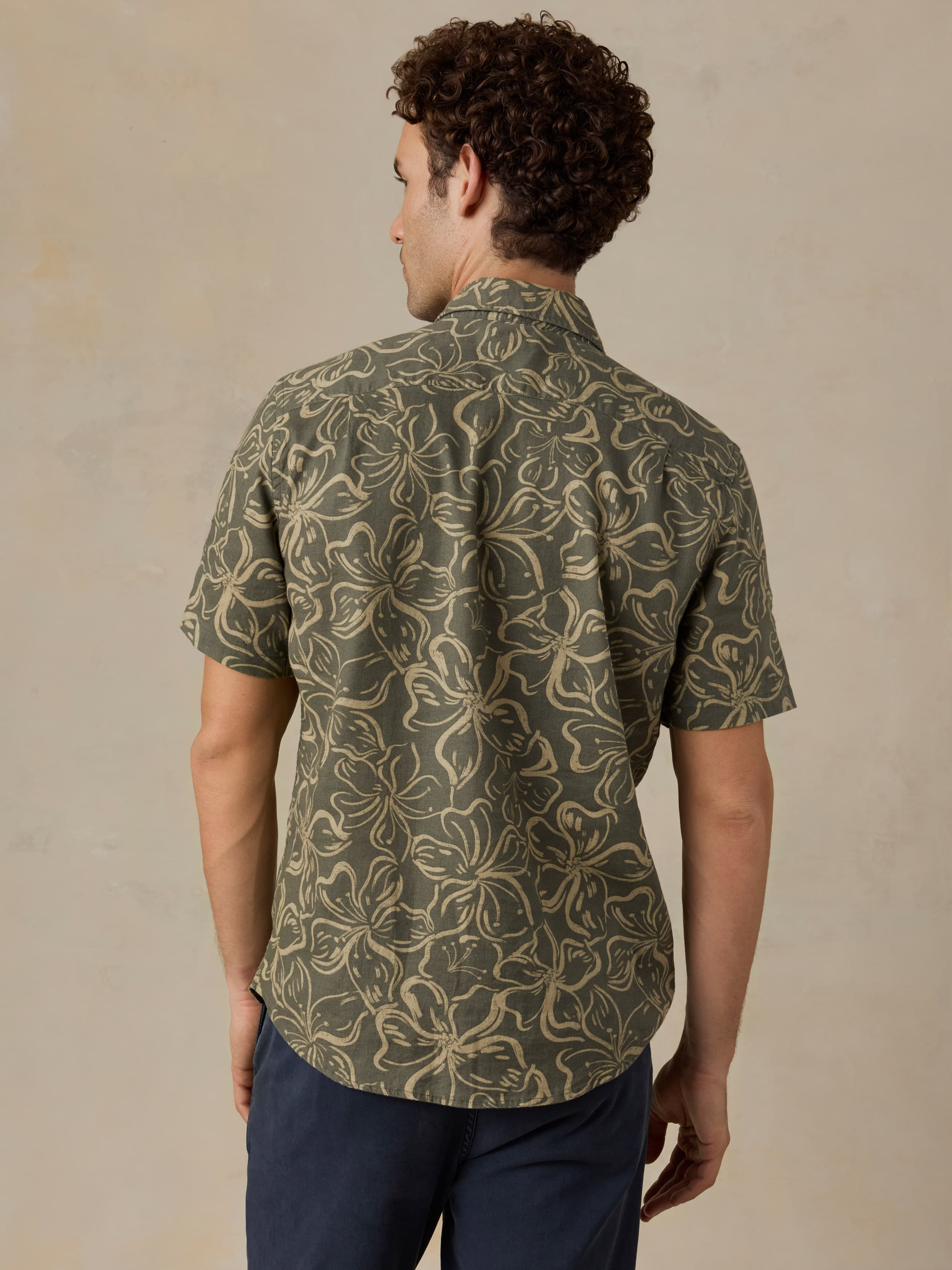 Man wearing a green floral printed shirt and navy pants against a beige background