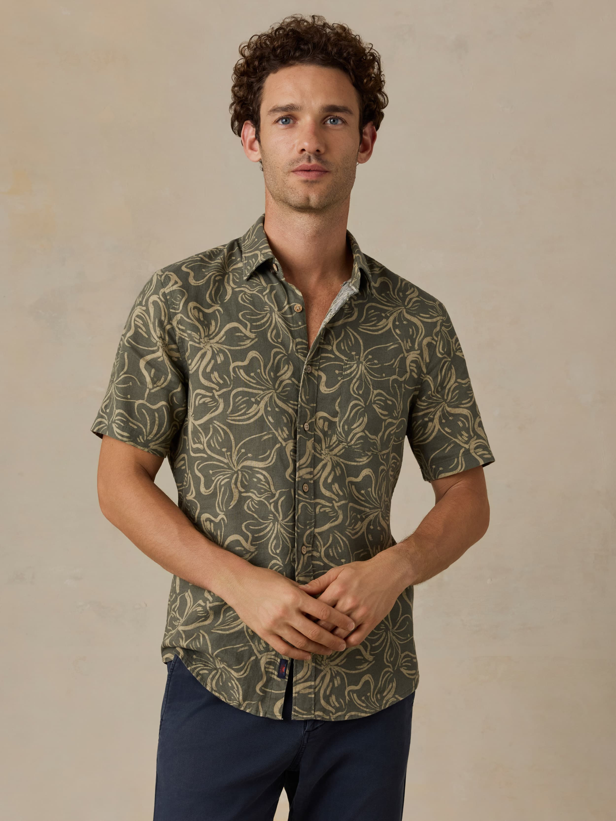 Man wearing a green floral printed shirt and navy pants against a beige background