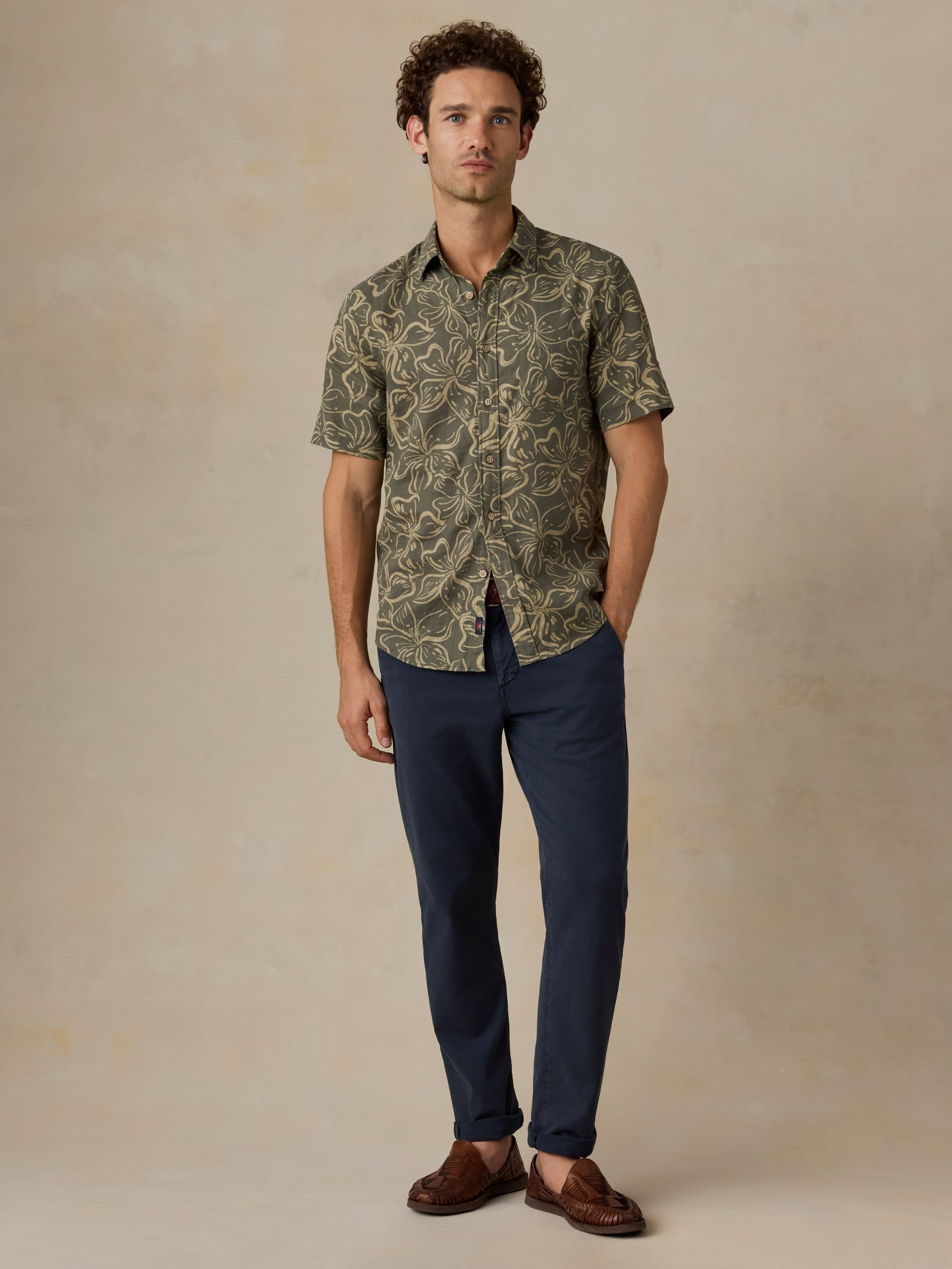 Man wearing a green floral printed shirt and navy pants against a beige background