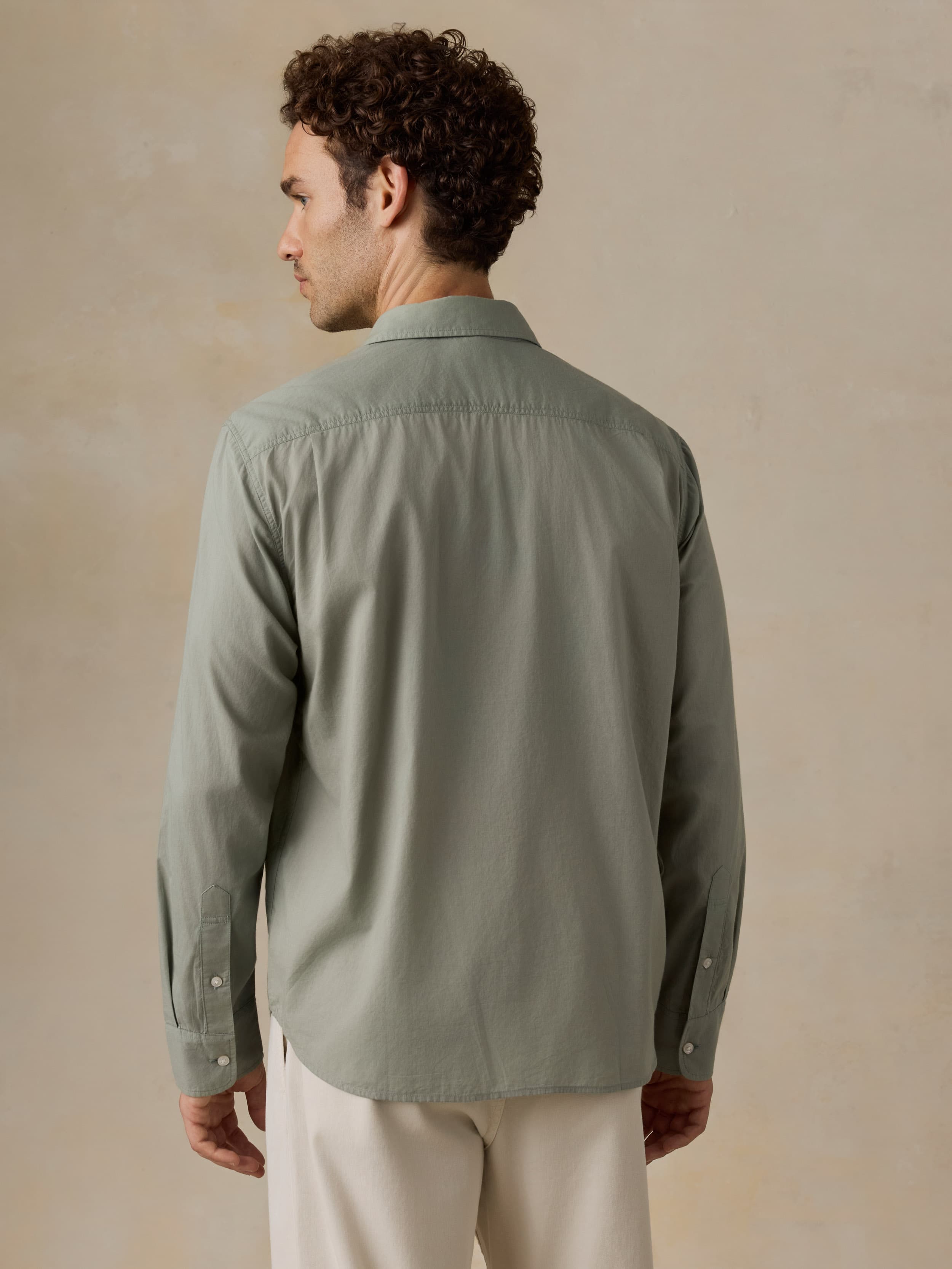 Man wearing a green shirt and beige pants against a beige background