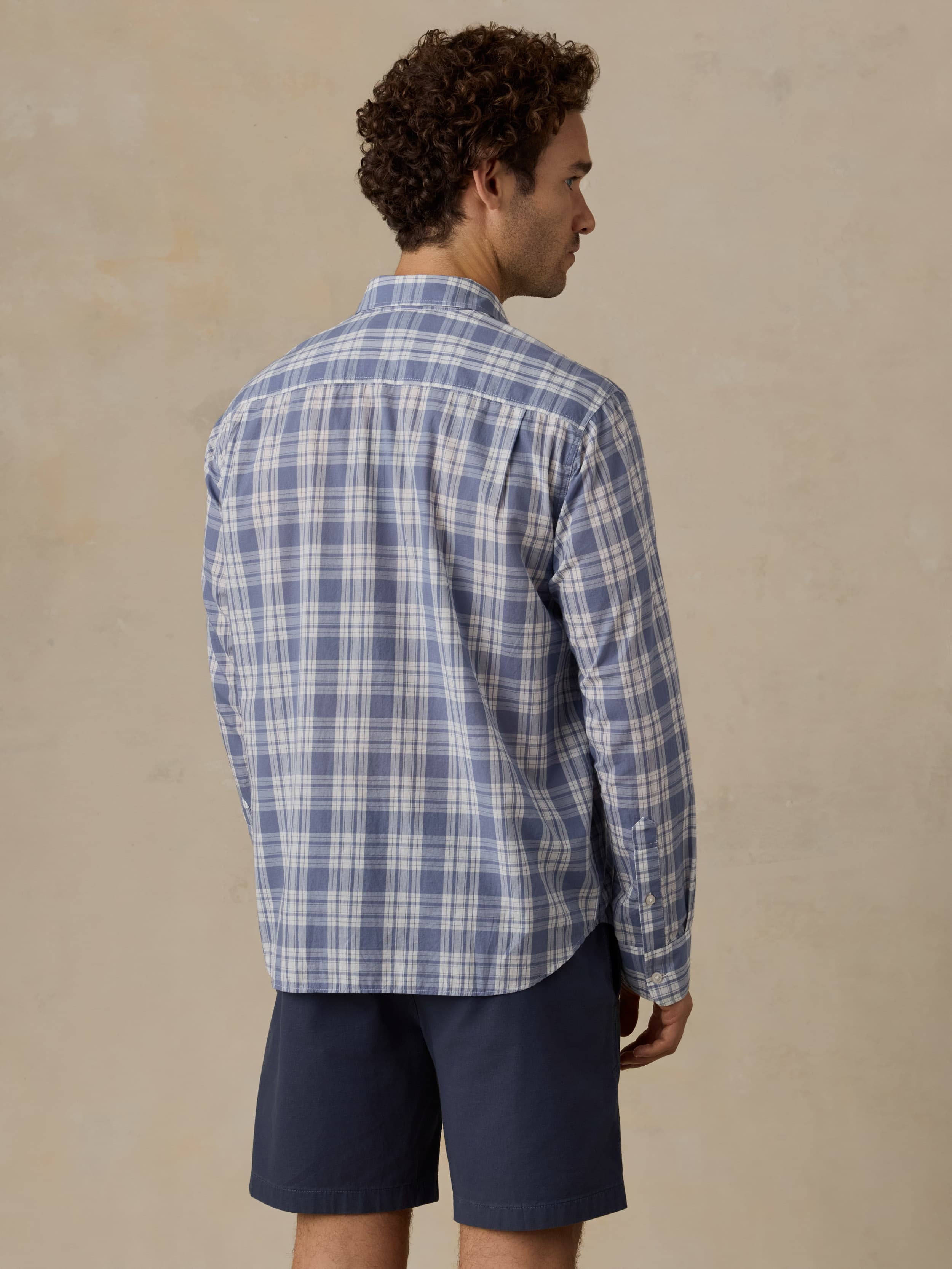 Man wearing a blue plaid shirt and navy short against a beige background
