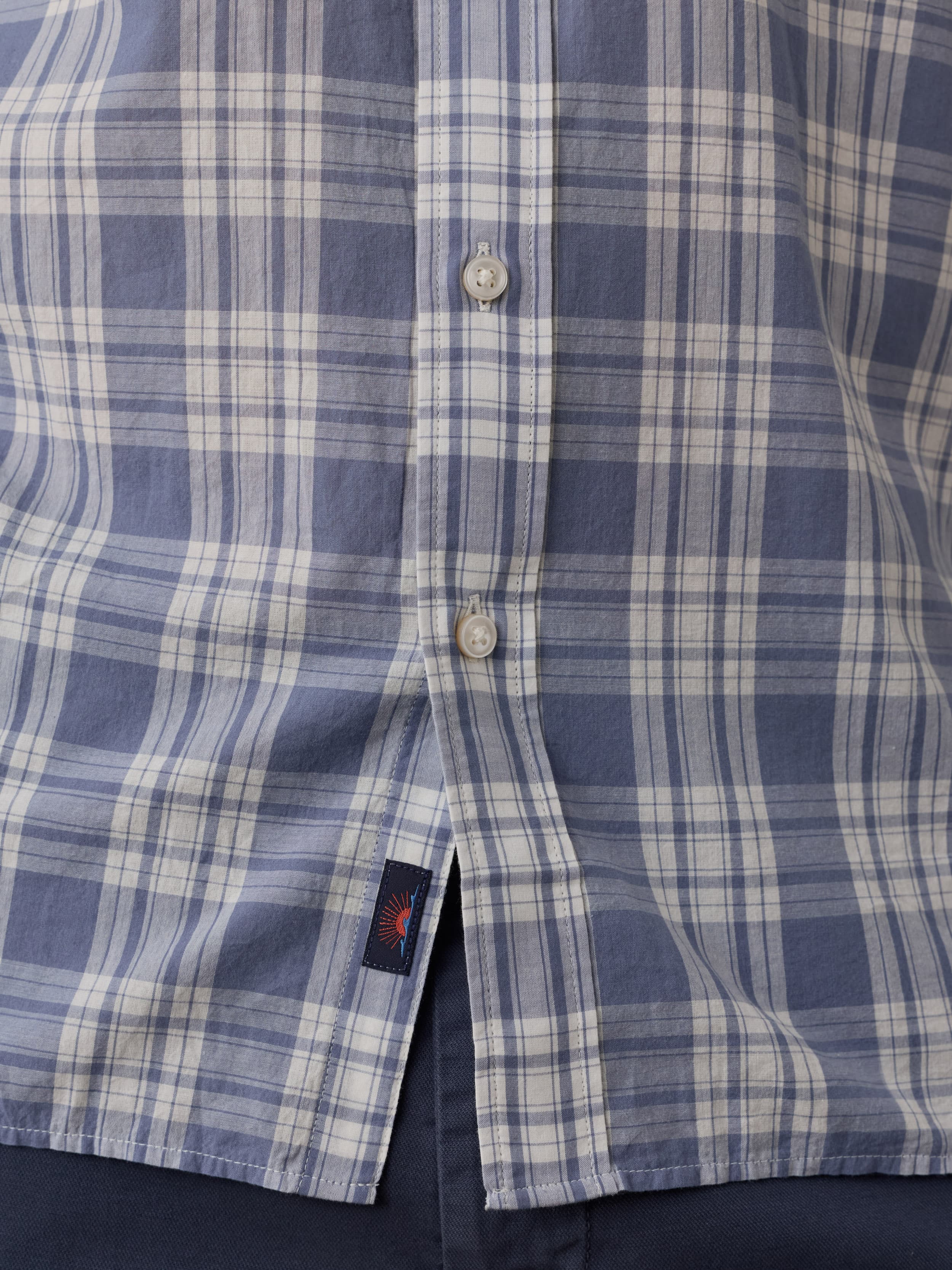 Close-up of a blue and white plaid shirt with a Faherty brand label near the hem