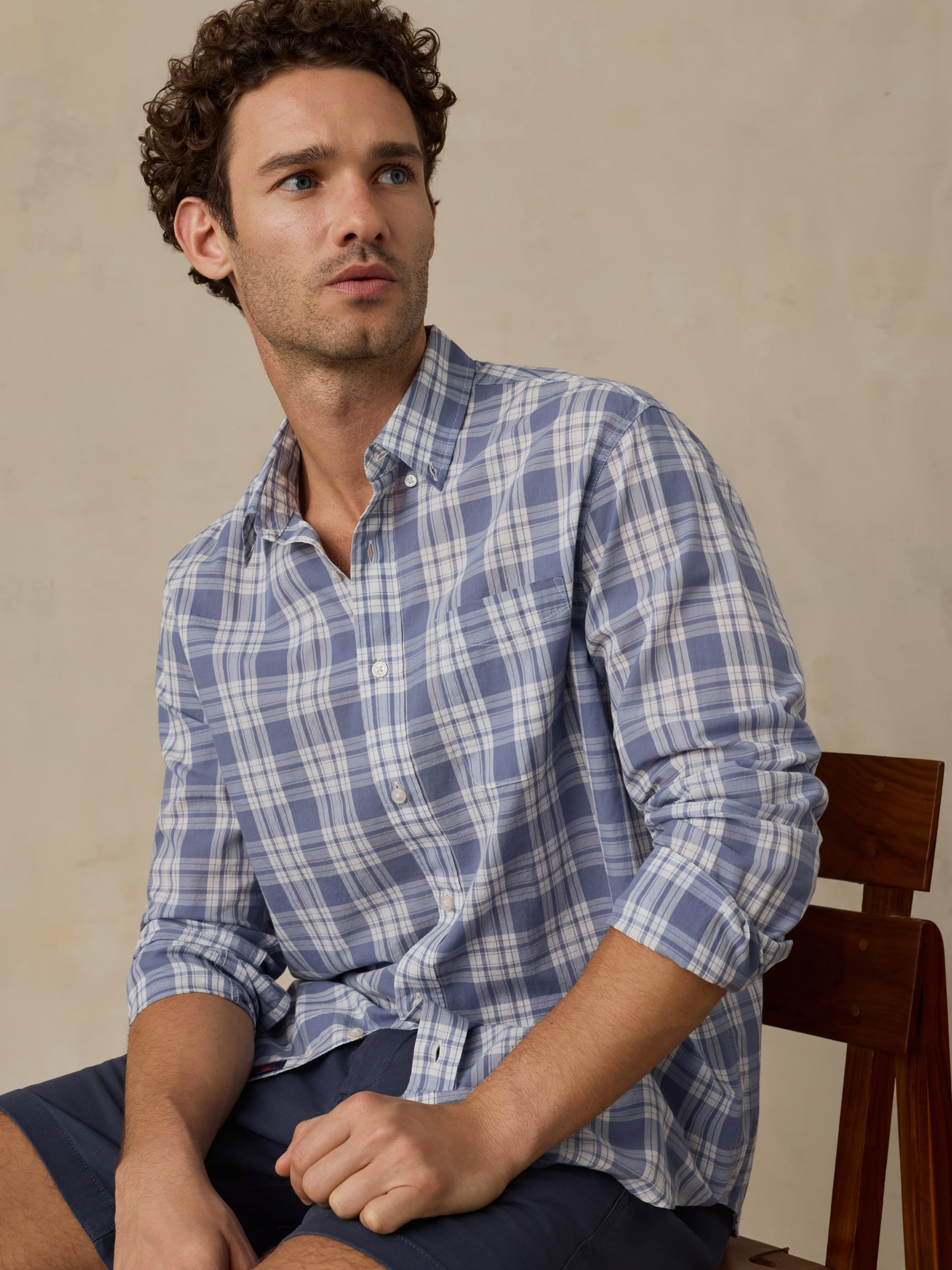 Man wearing a blue plaid shirt and navy short against a beige background