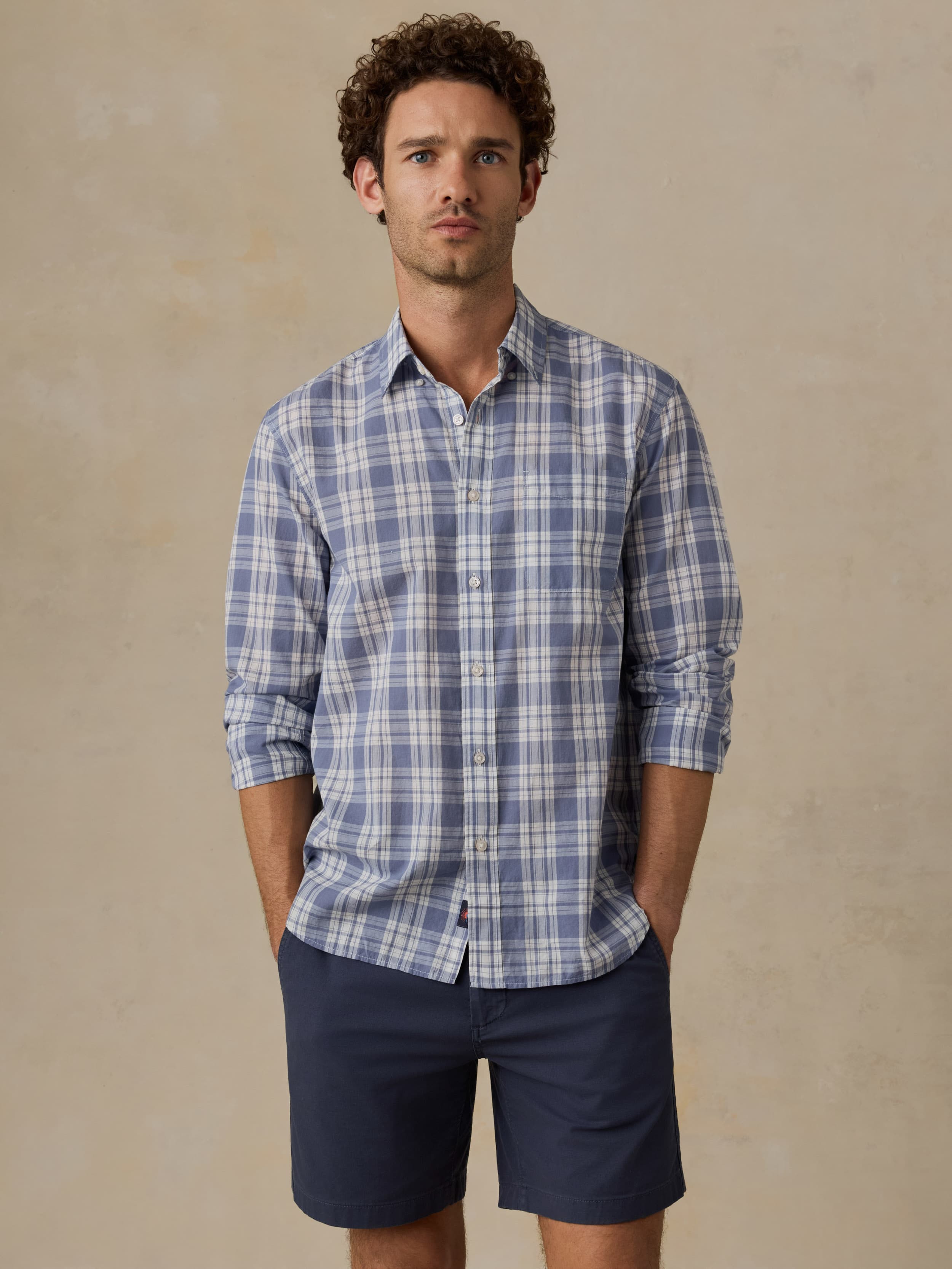 Man wearing a blue plaid shirt and navy short against a beige background