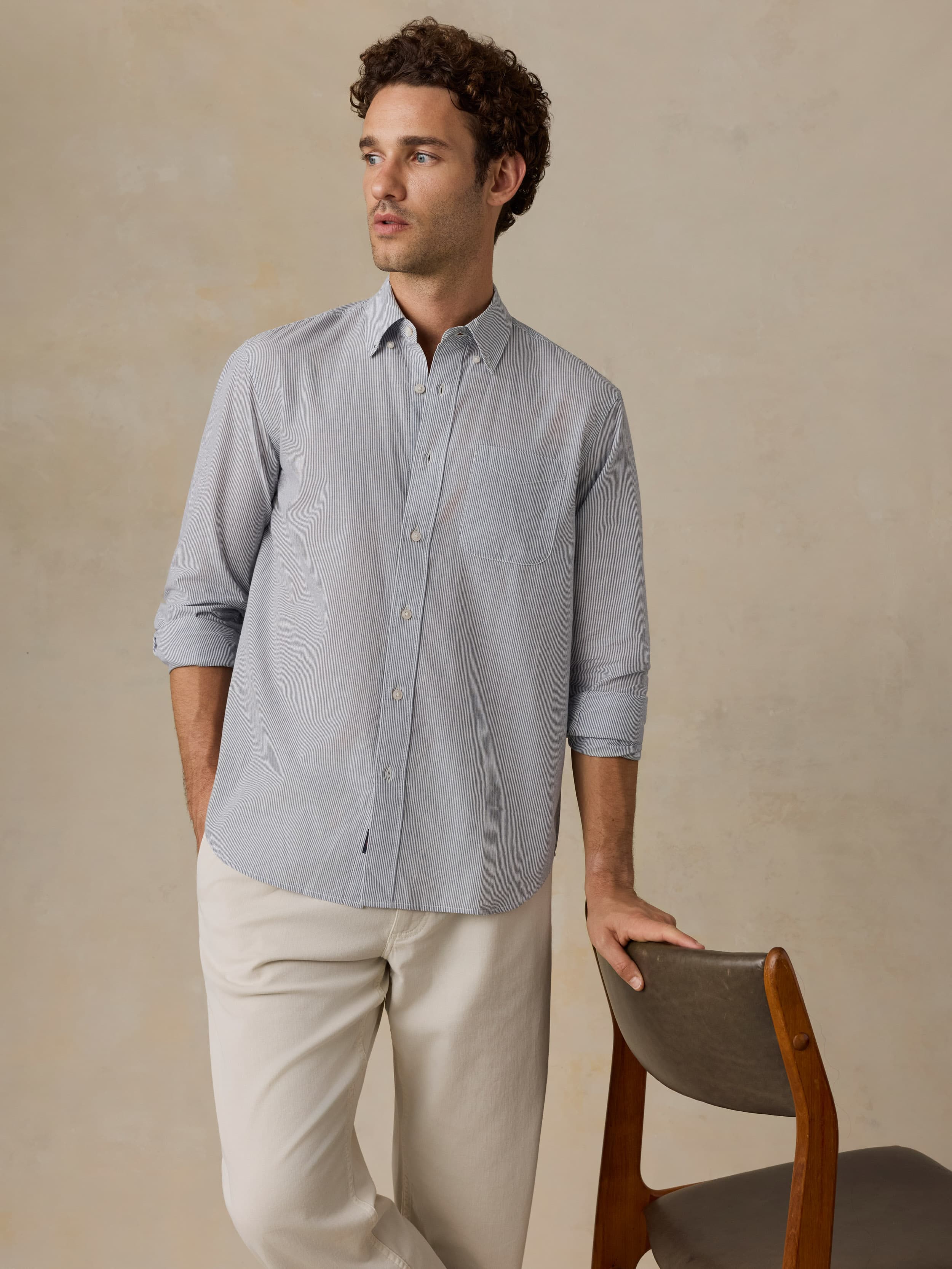 Man wearing a light blue shirt and white pants against a beige background