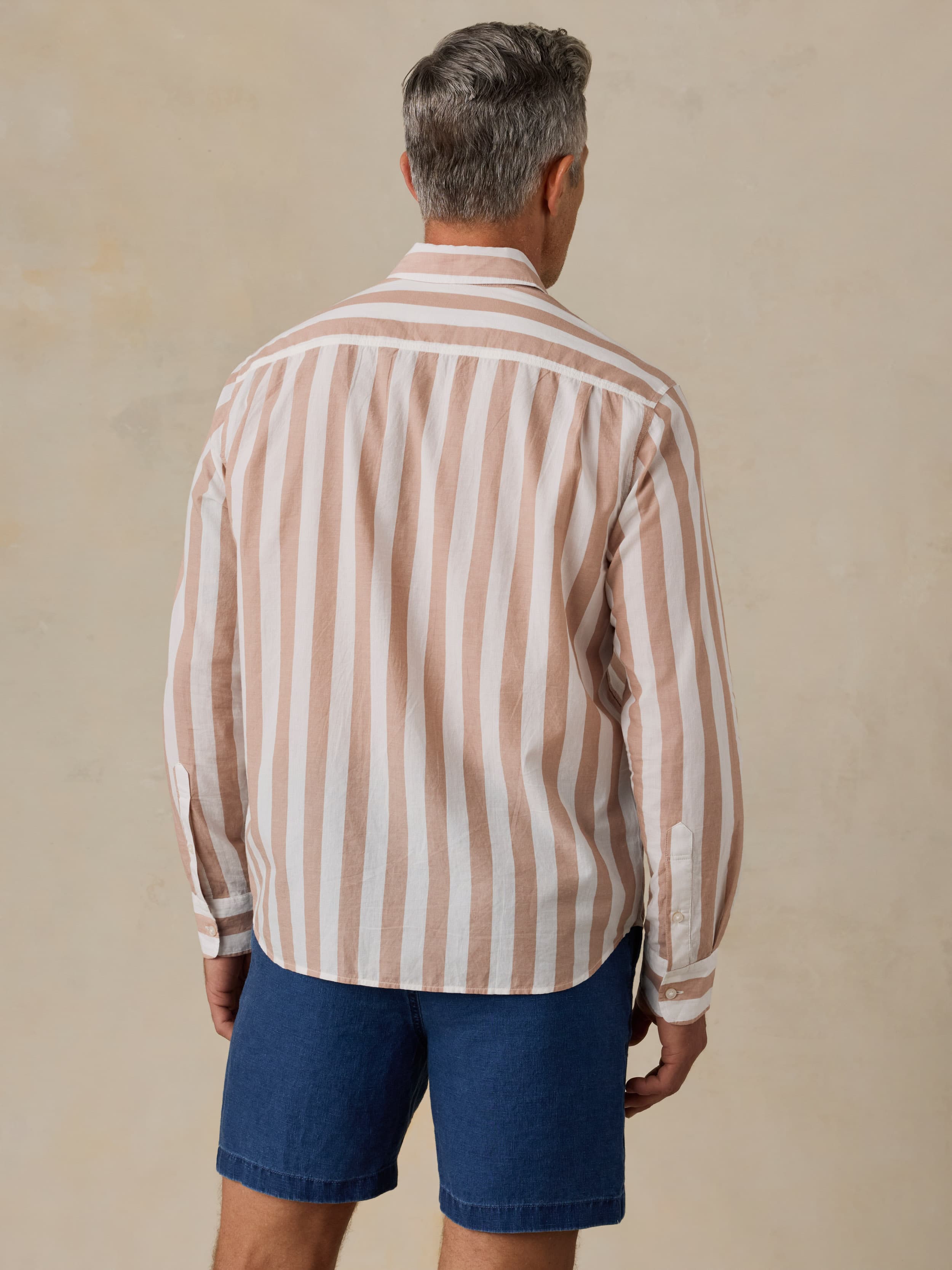Man wearing a striped shirt and blue shorts against a beige background