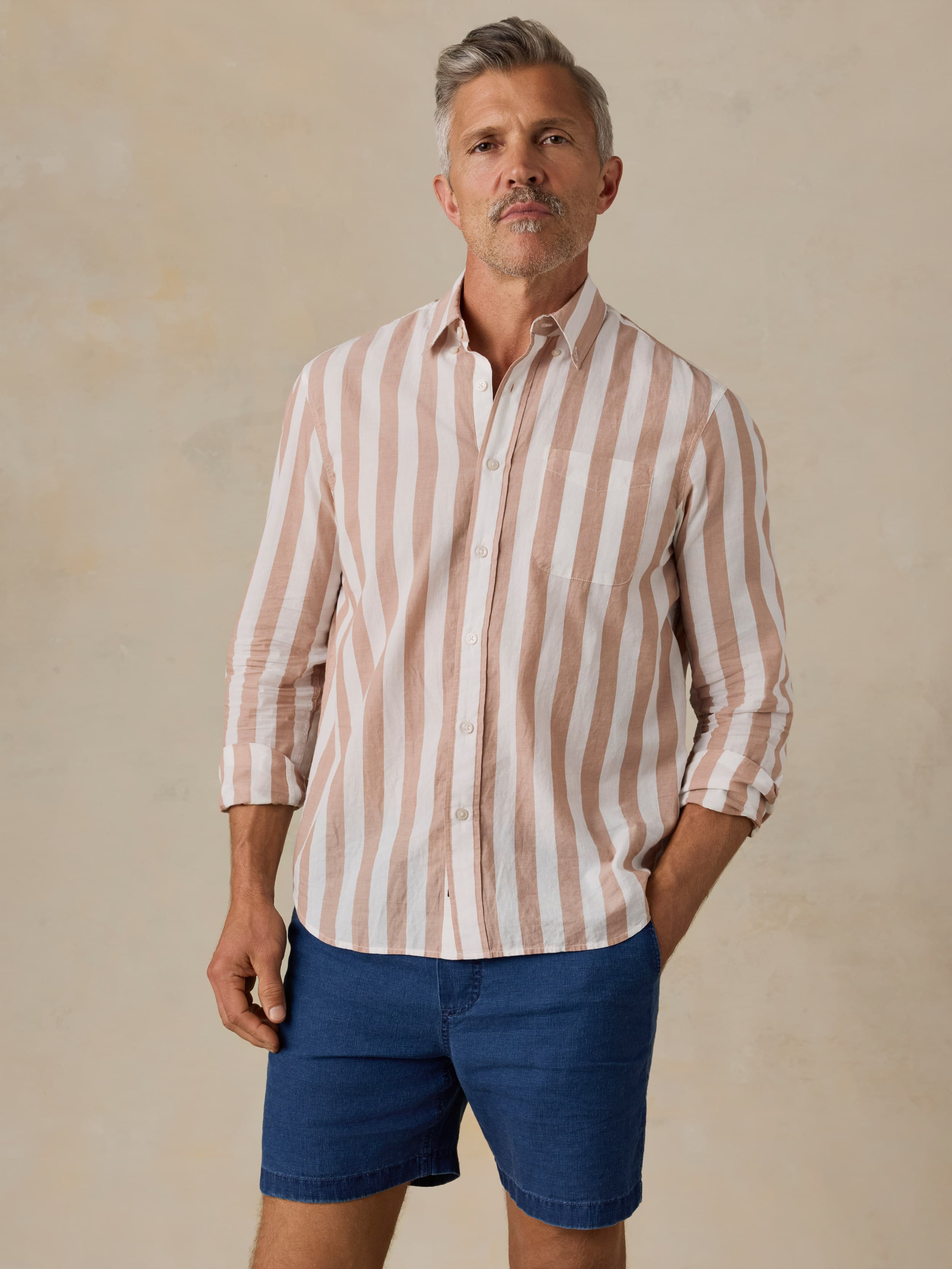 Man wearing a striped shirt and blue shorts against a beige background