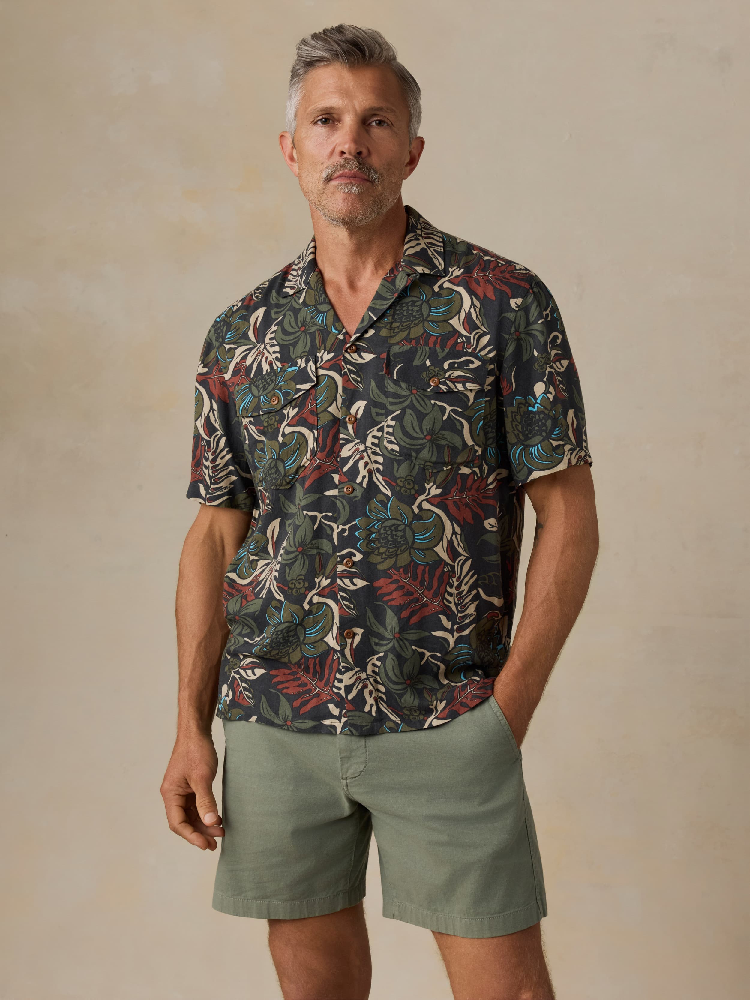 Man wearing a tropical patterned shirt and green shorts against a beige background