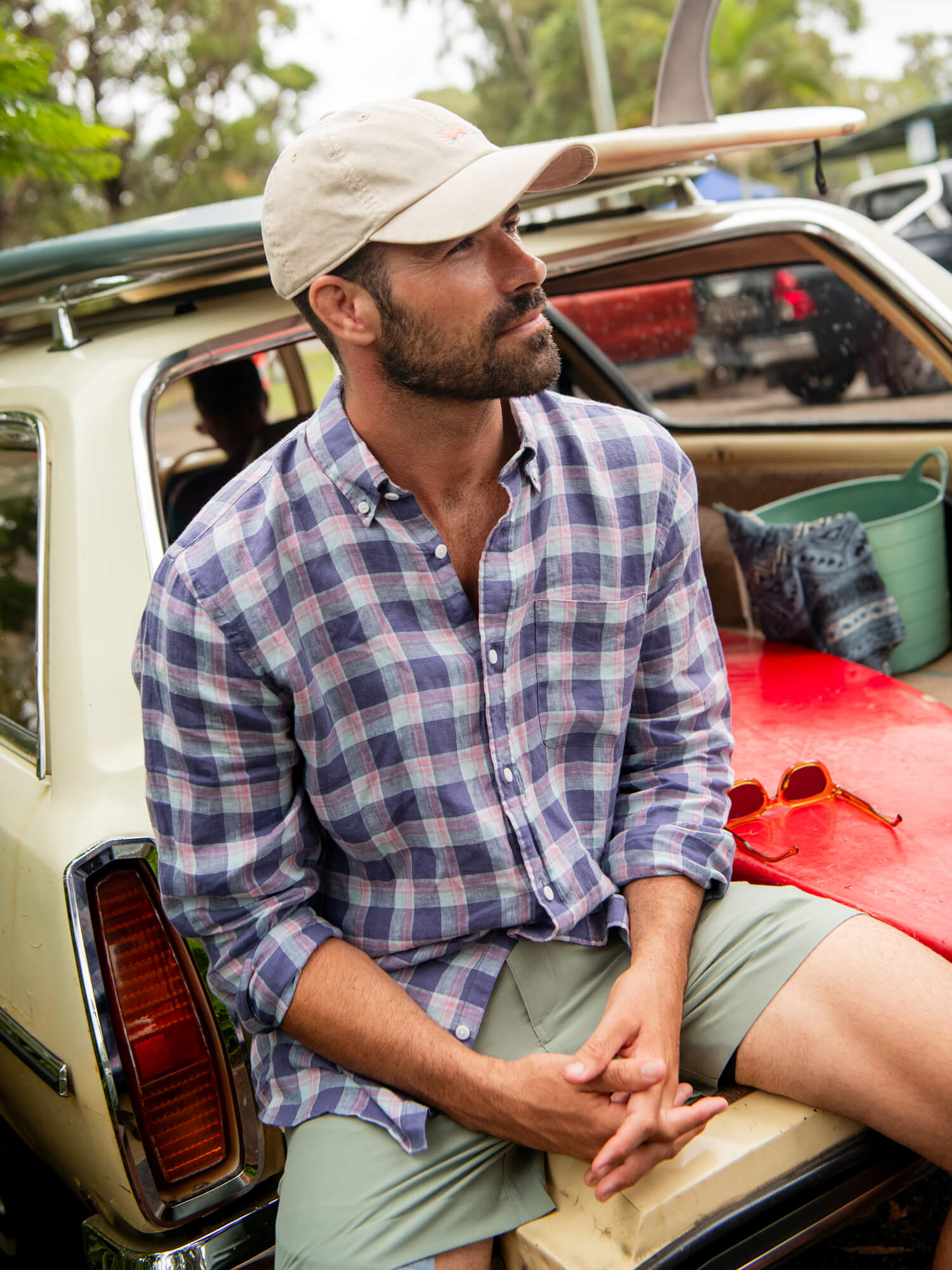 Man wearing a plaid long sleeve shirt and green shorts sitting in the back of a vintage car