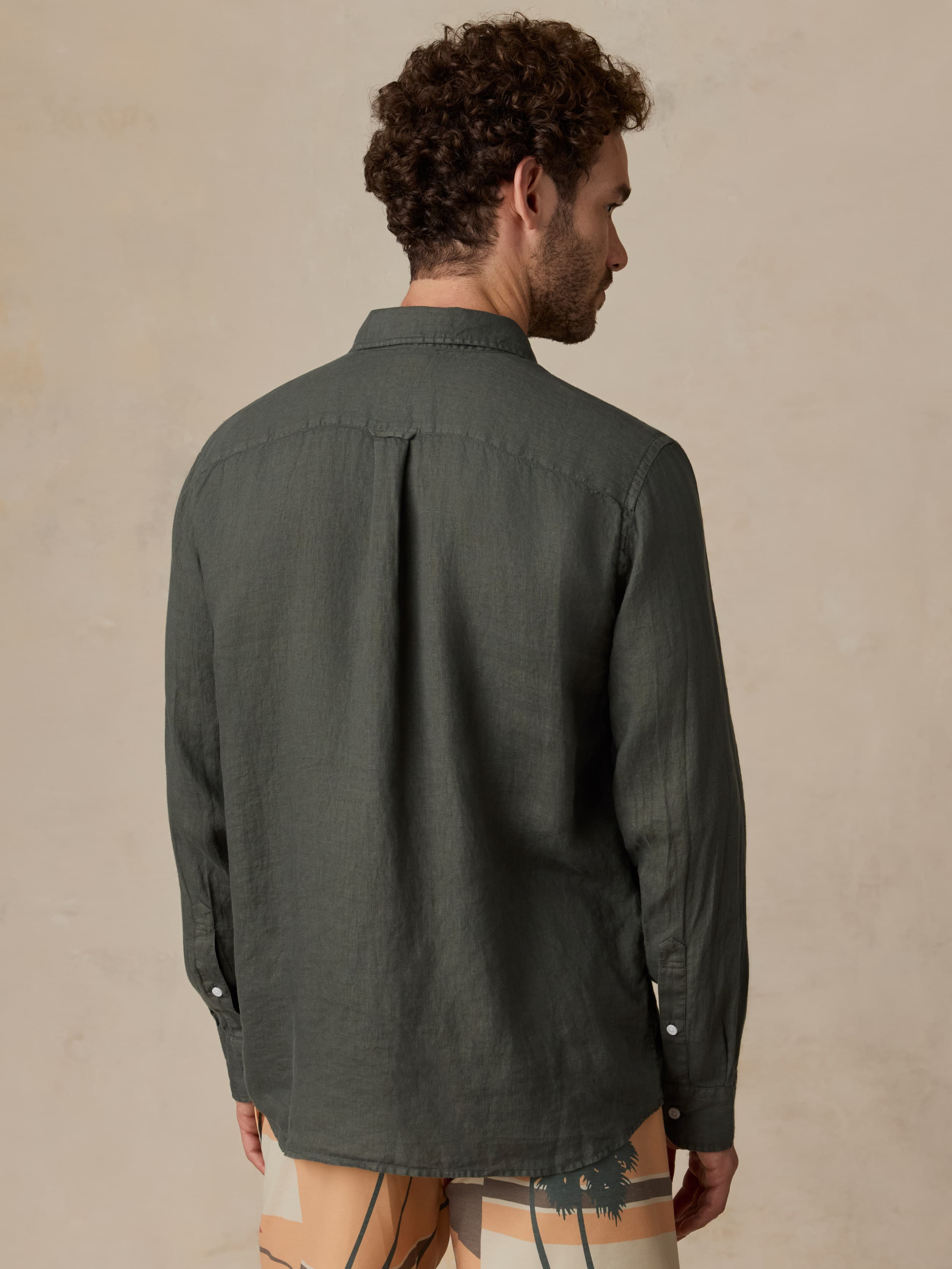 Man wearing a green linen shirt and printed swim shorts against a beige background