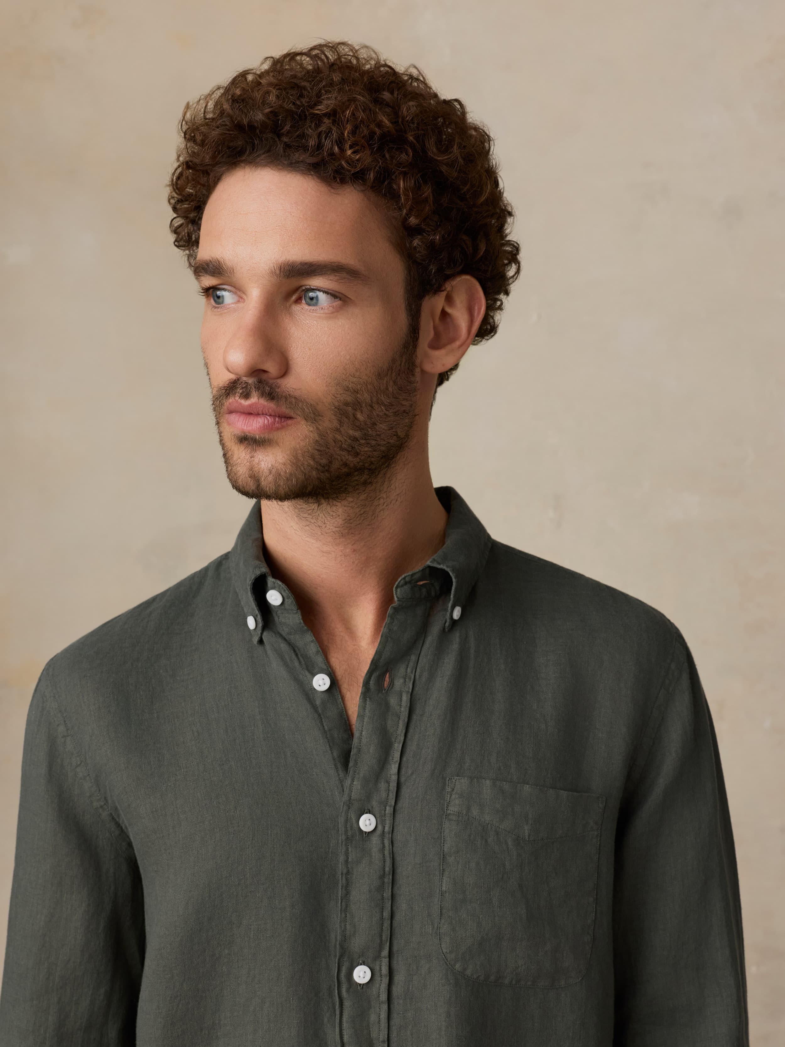 Man wearing a green linen shirt and printed swim shorts against a beige background