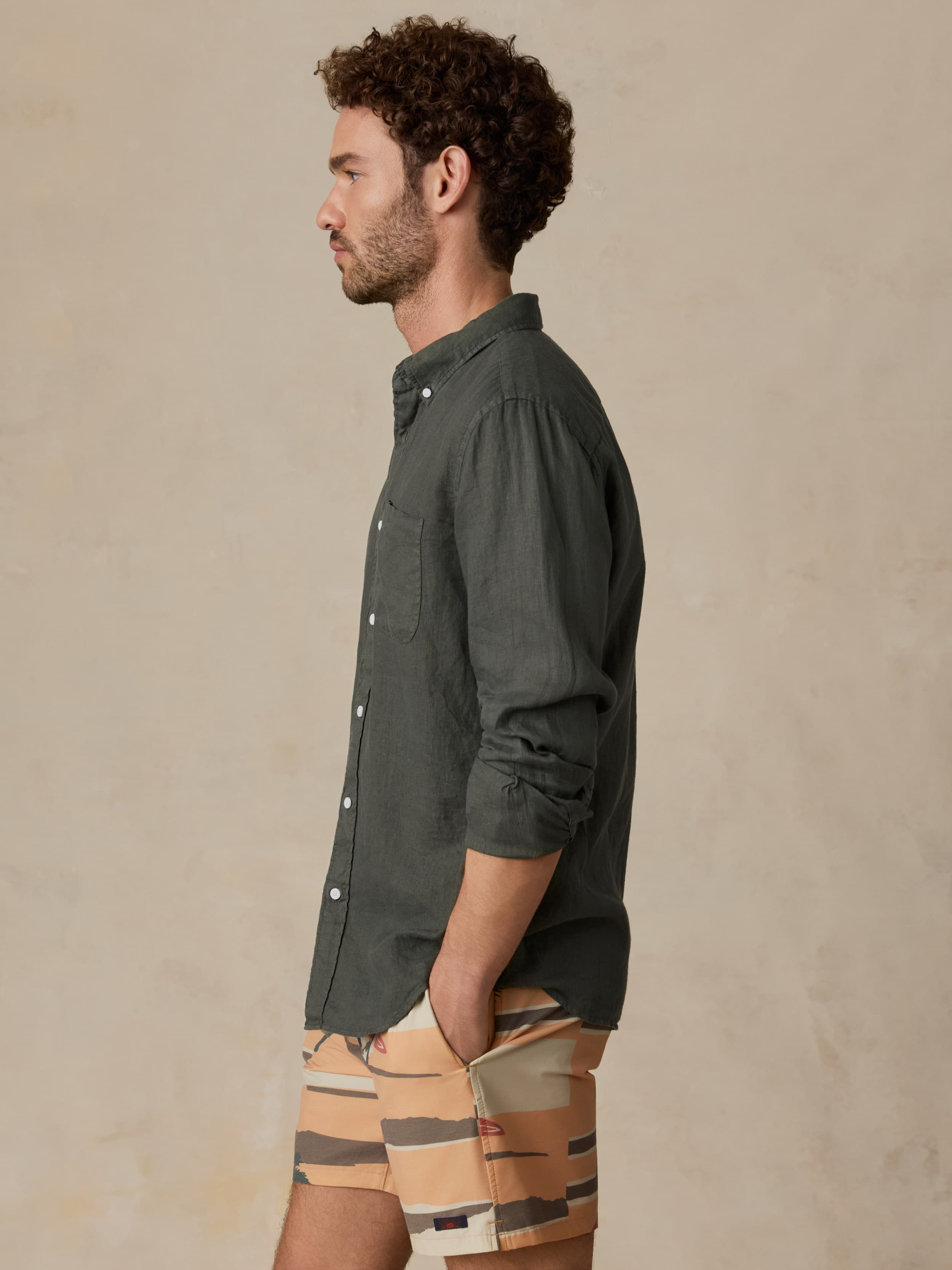 Man wearing a green linen shirt and printed swim shorts against a beige background