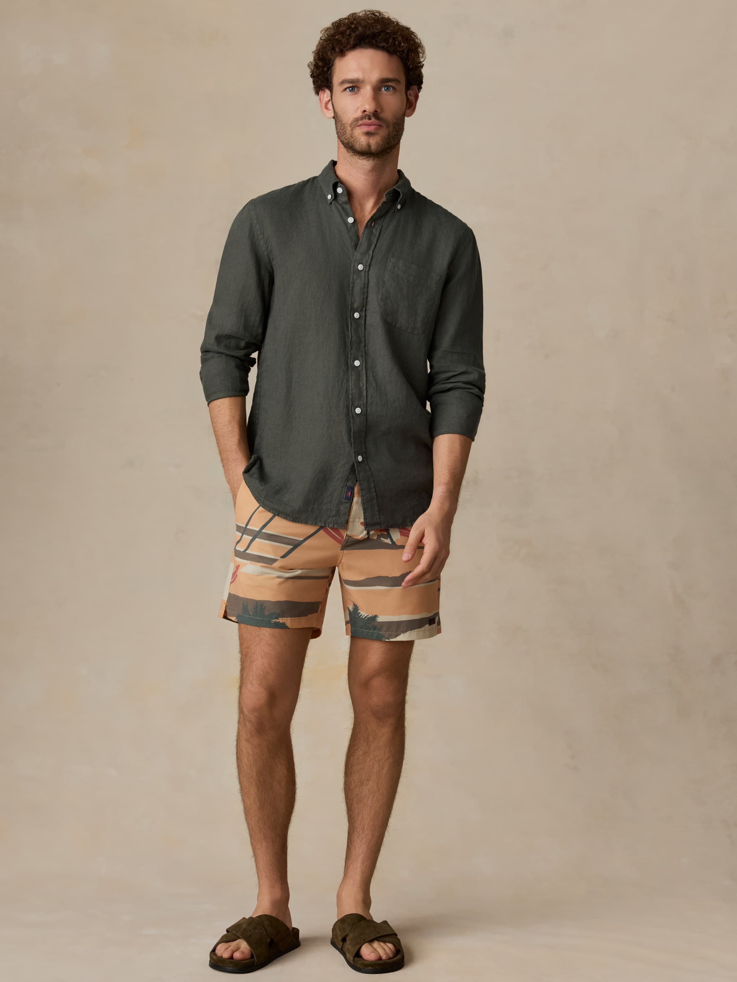 Man wearing a green linen shirt and printed swim shorts against a beige background