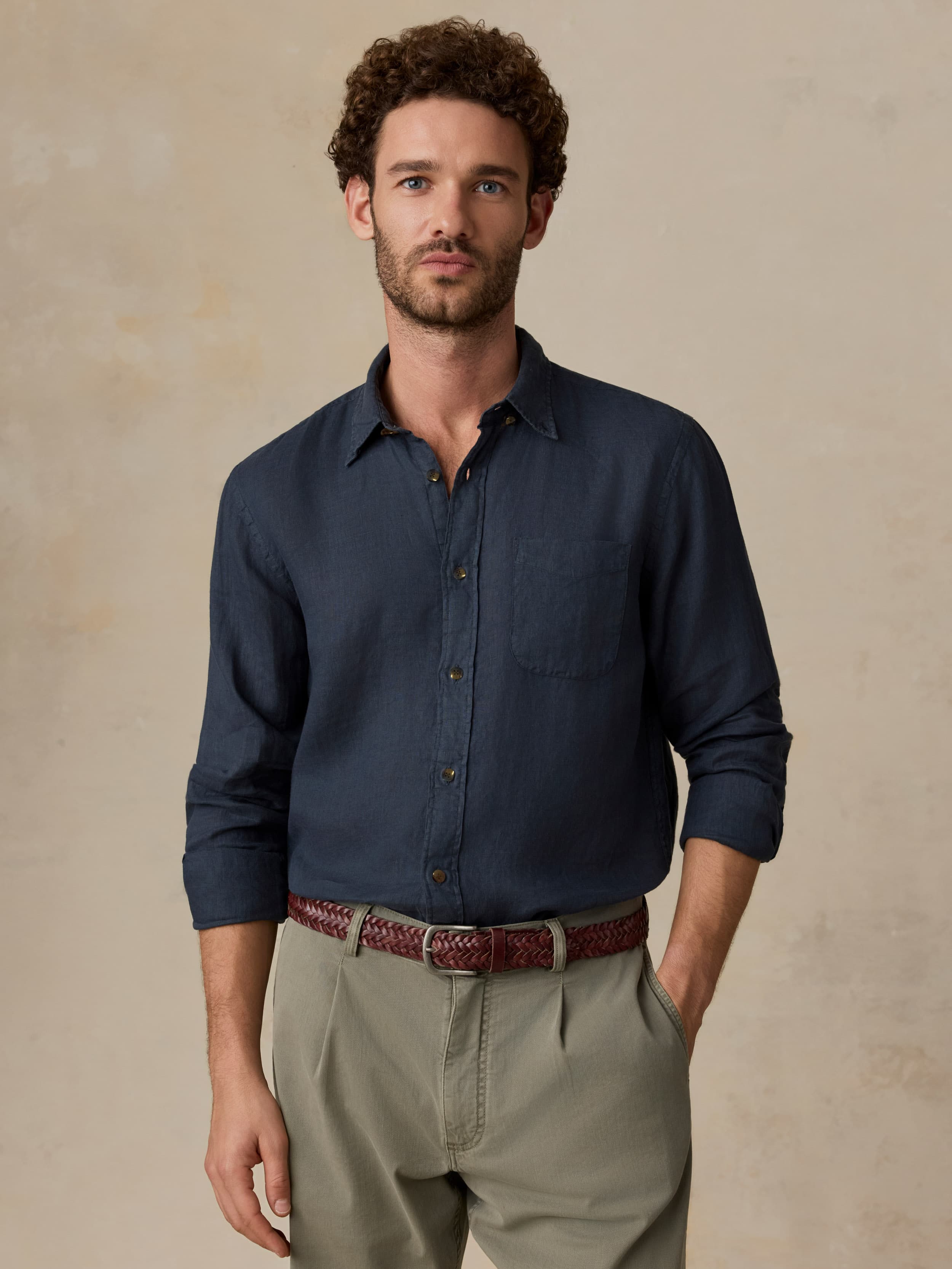 Man wearing a navy shirt and beige pants against a beige background
