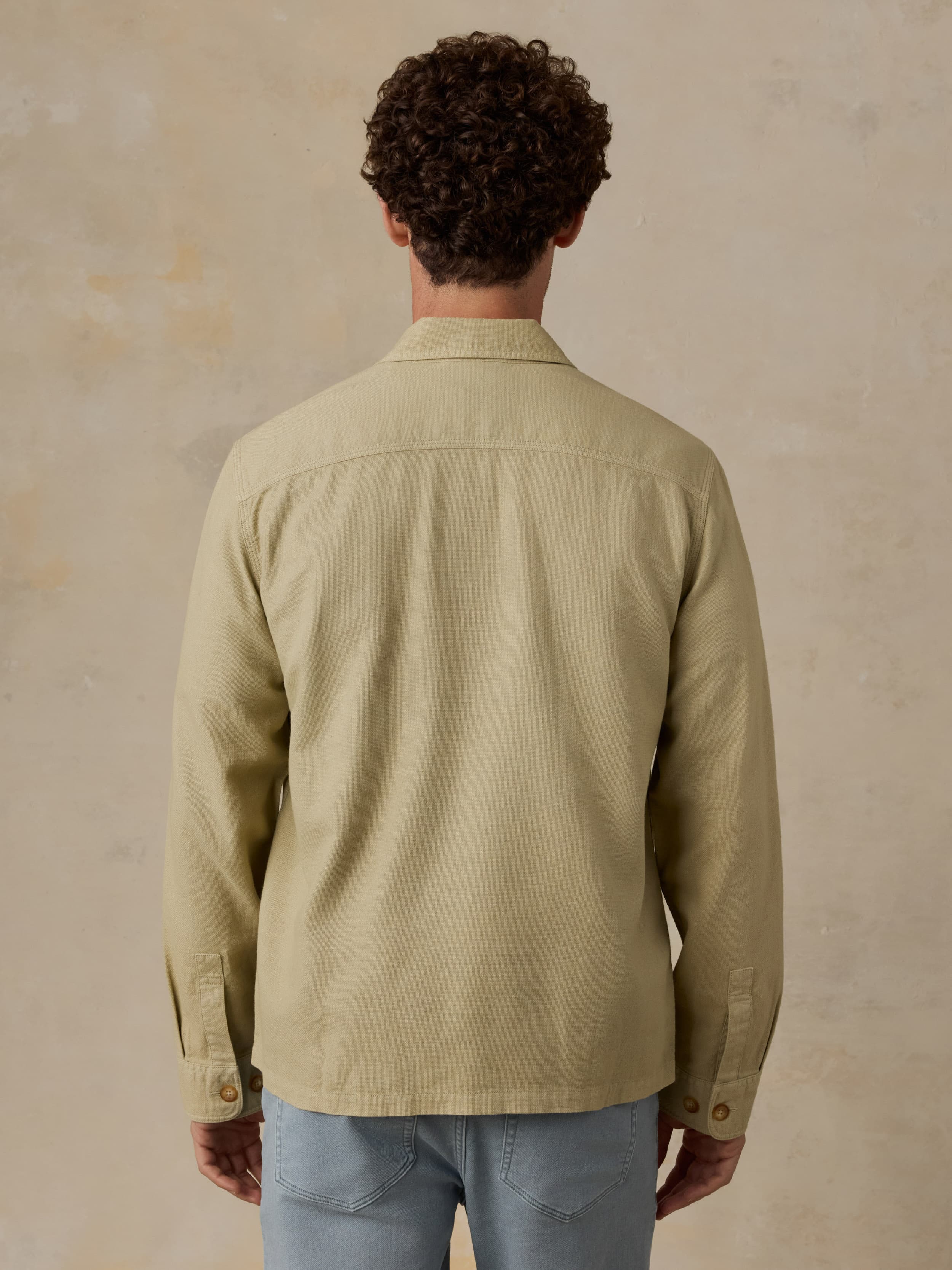 Man wearing a beige button down shirt with blue jeans against a beige background
