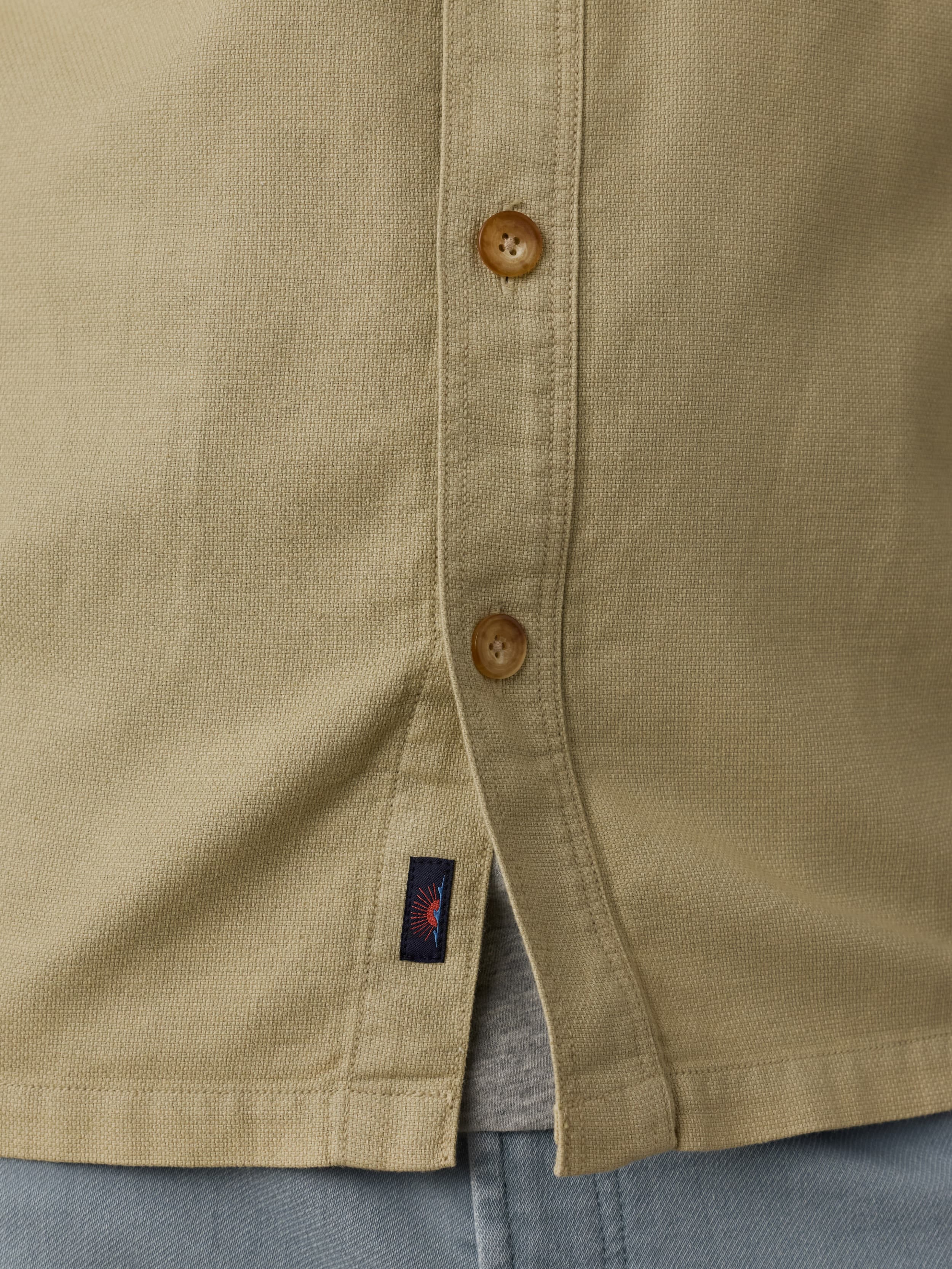 Close up of a man wearing a beige shirt with button details and Faherty brand label near the hem