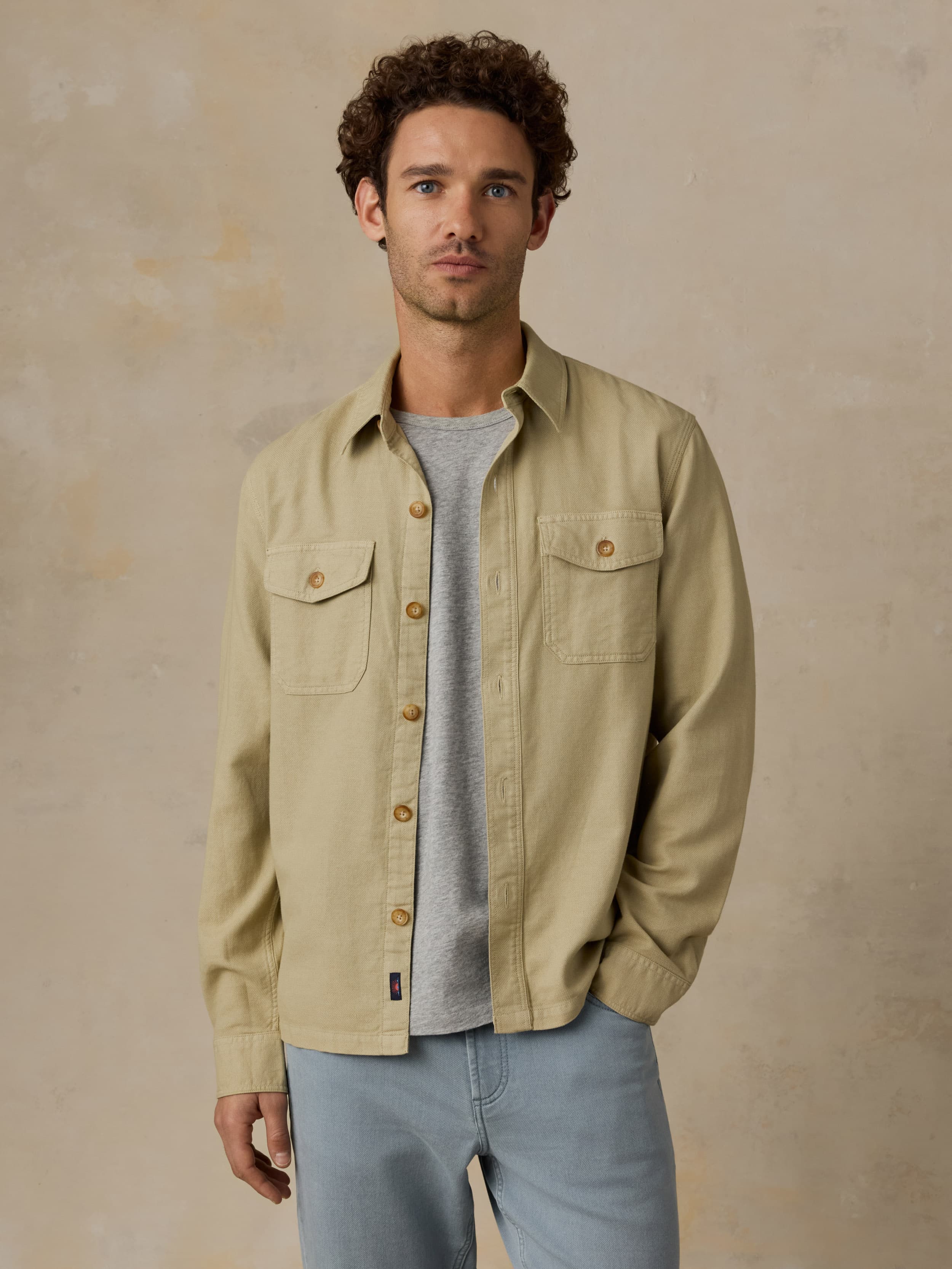 Man wearing a beige button down shirt with blue jeans against a beige background