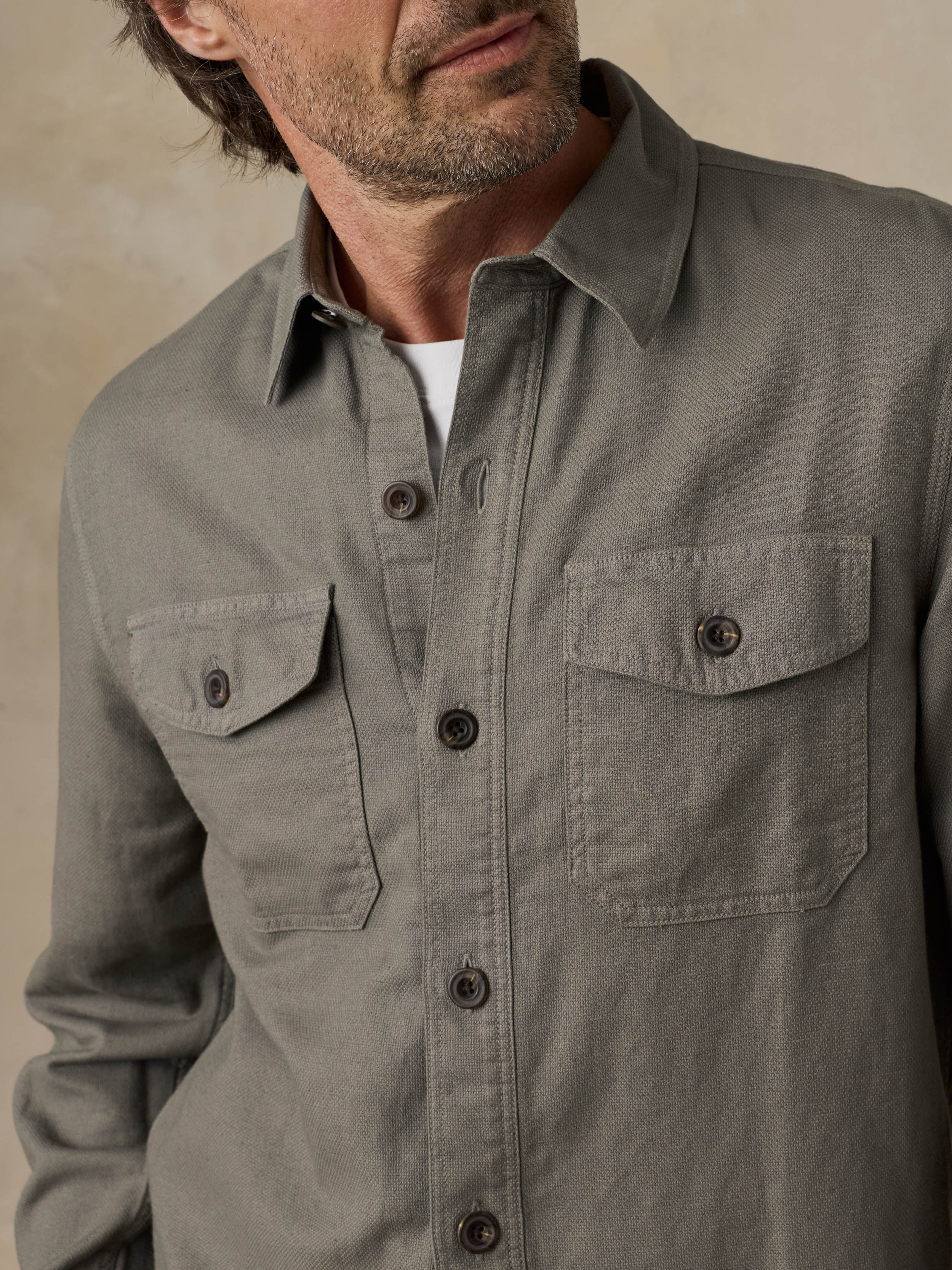 Man wearing an olive green button-up shirt with two front pockets on a beige background
