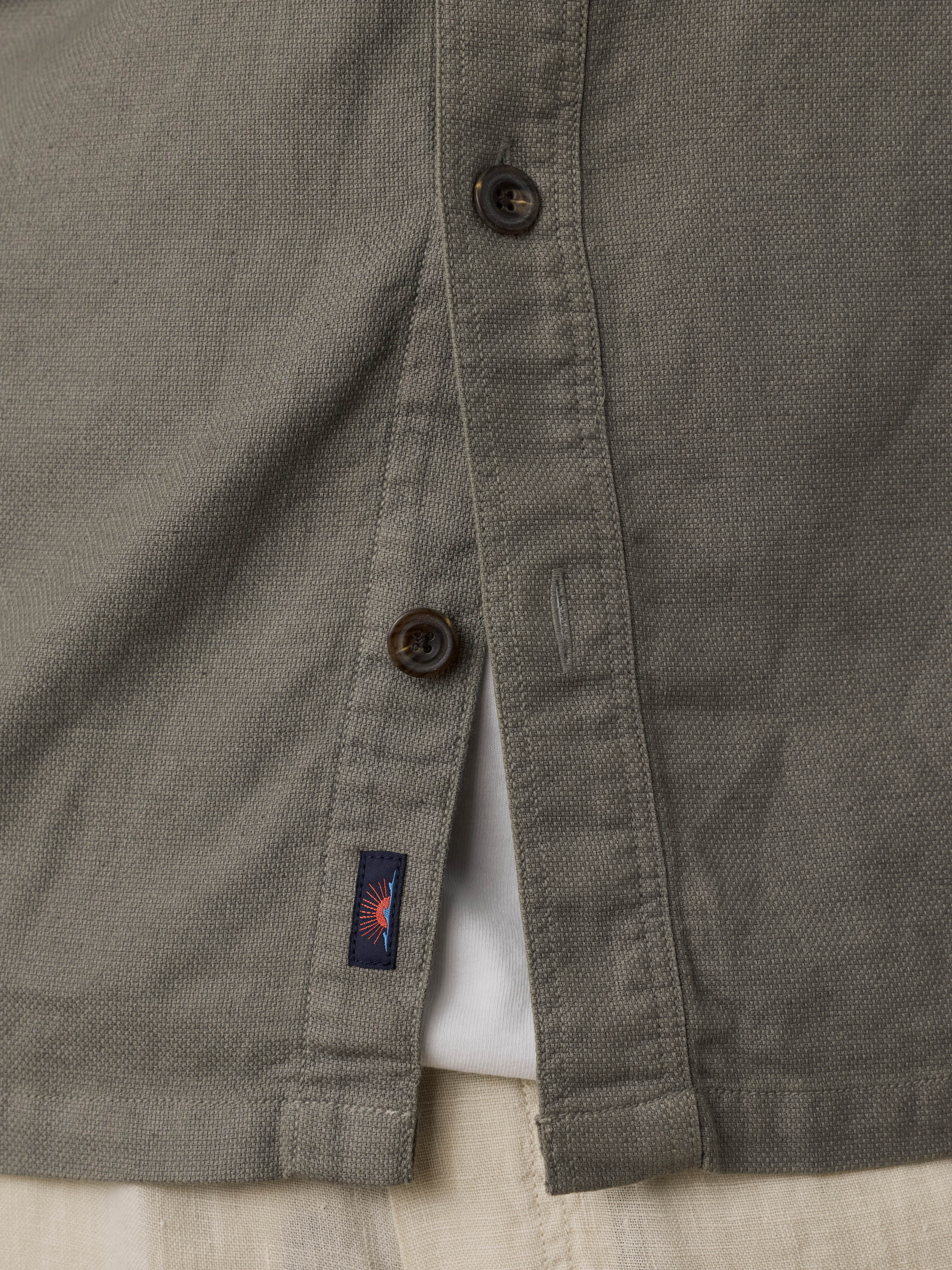 Close-up of an olive green shirt with buttons and a Faherty brand label