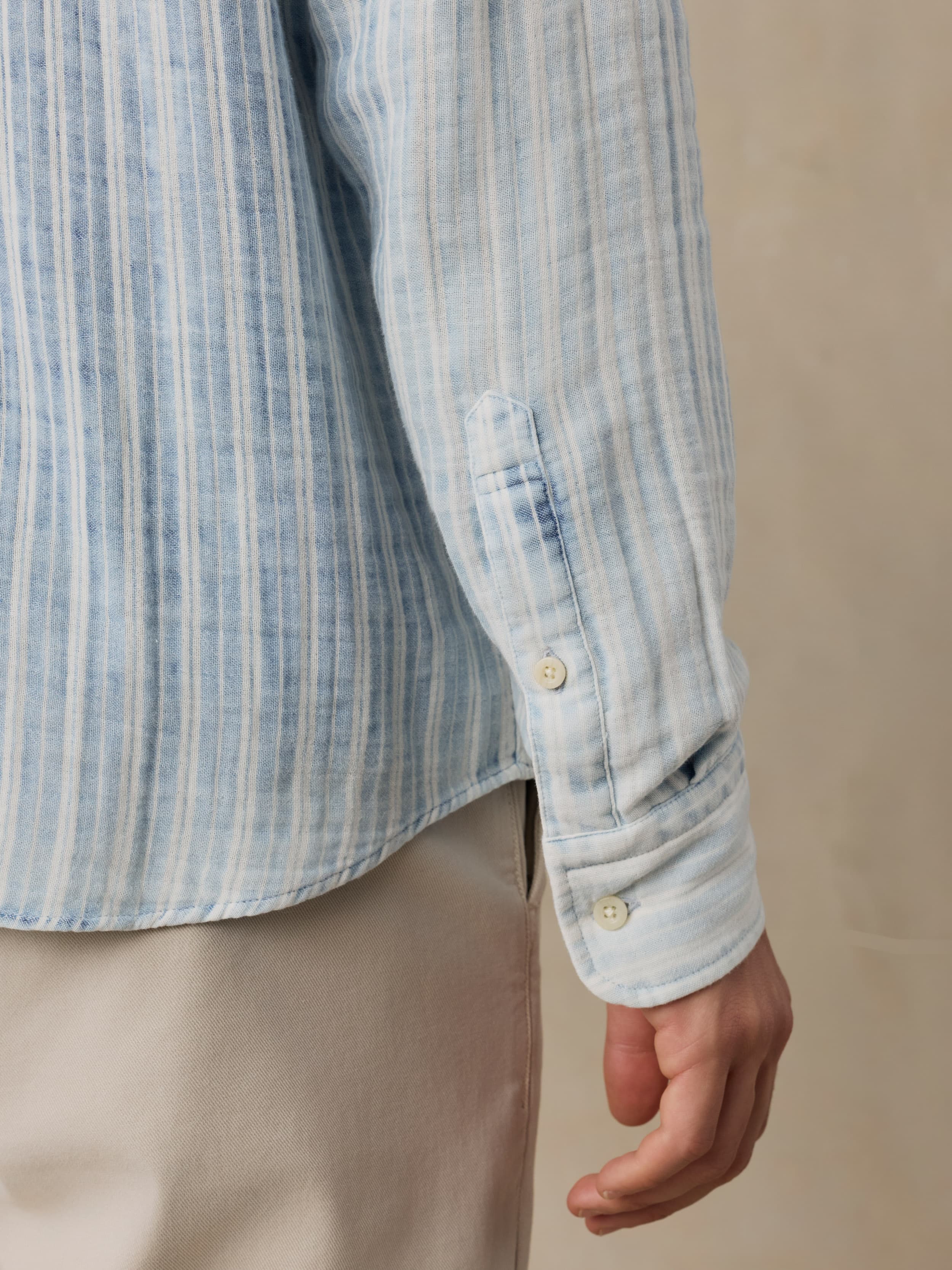 Close-up of a man wearing a light blue striped shirt with beige pants on a beige background
