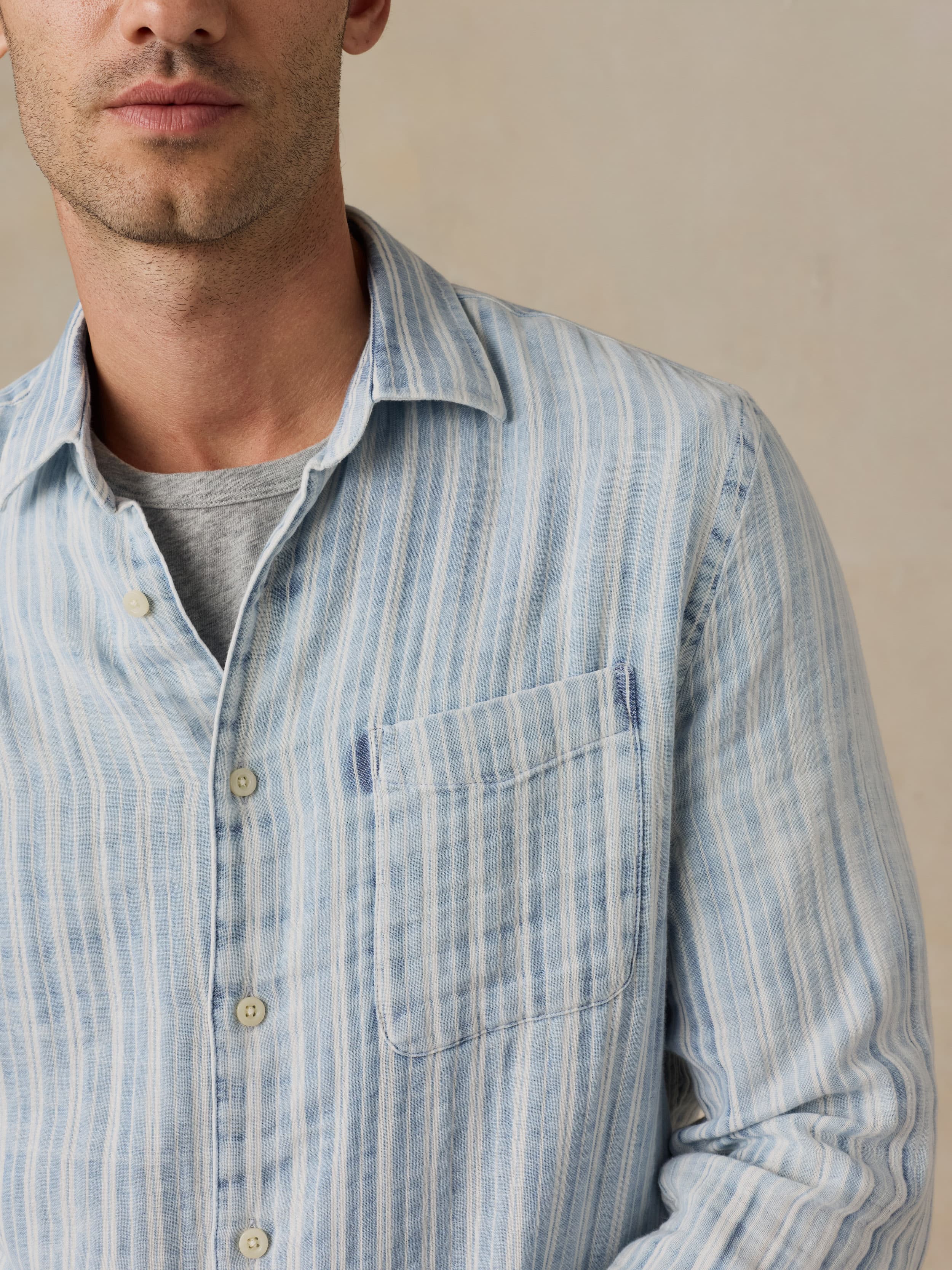 Man wearing a light blue striped shirt against a beige background