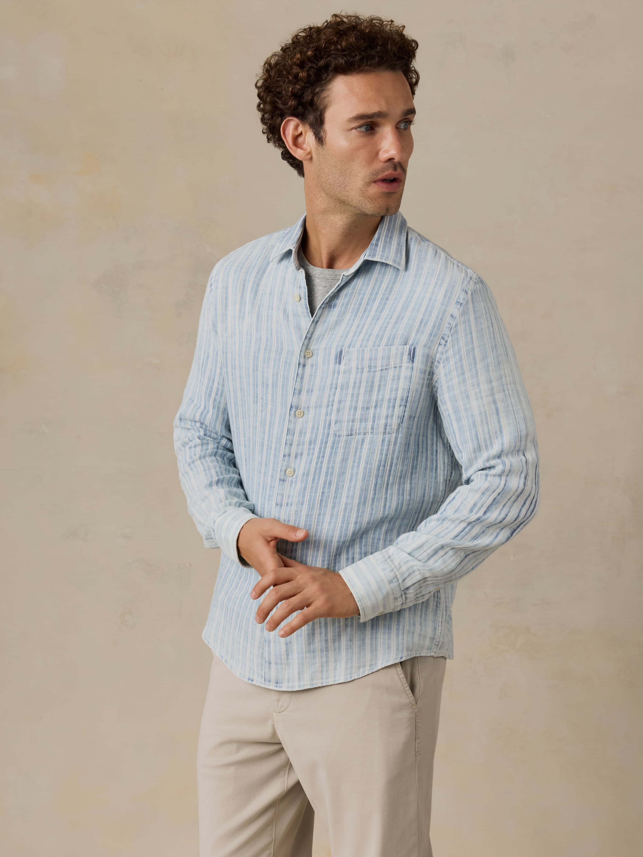 Man wearing a light blue striped shirt and beige pants against a beige background