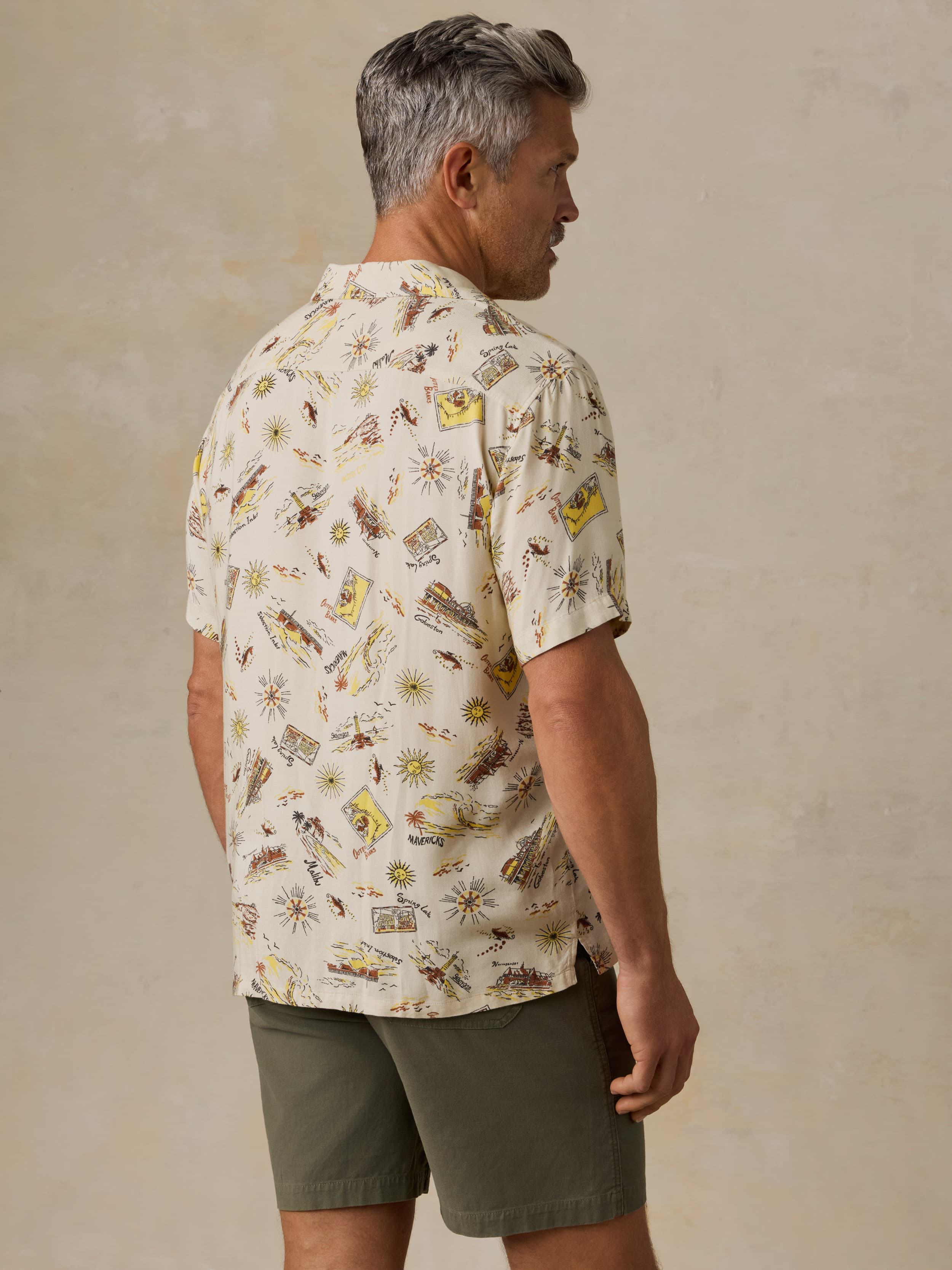 Man wearing a patterned shirt and green shorts against a beige background