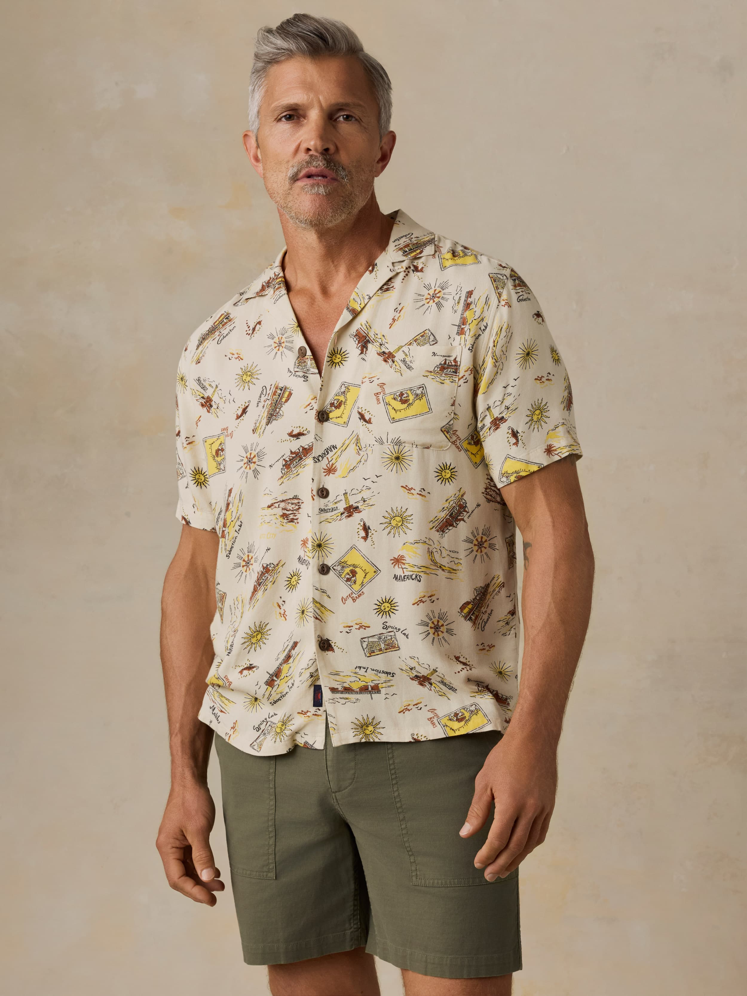 Man wearing a patterned shirt and shorts against a beige background