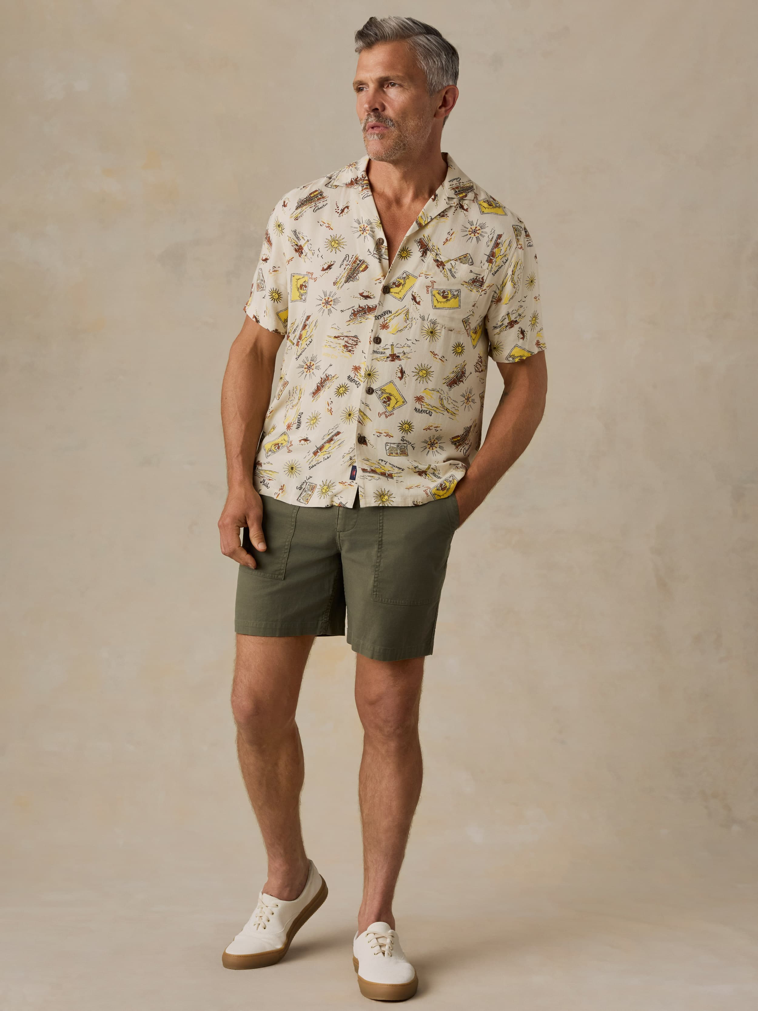 Man wearing a patterned shirt and shorts against a beige background