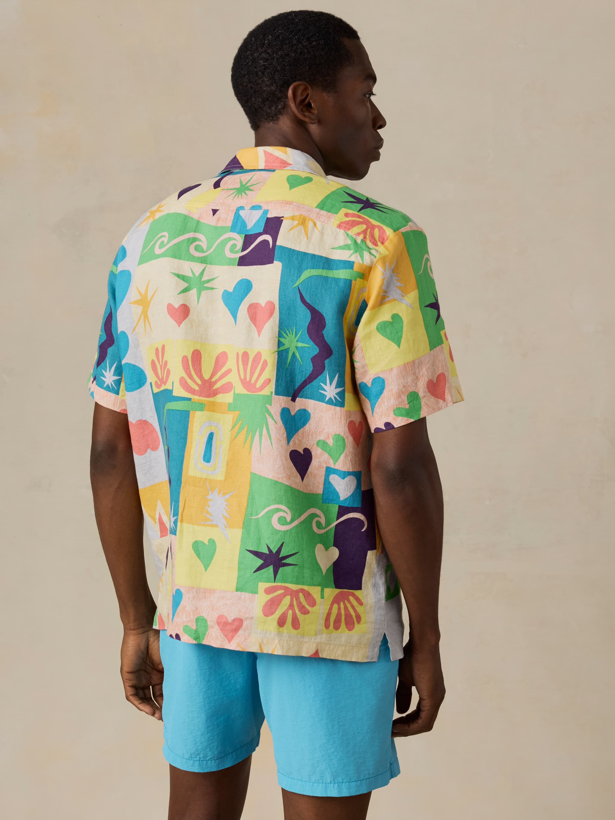 Man wearing a colorful printed shirt and blue swim shorts against a beige background