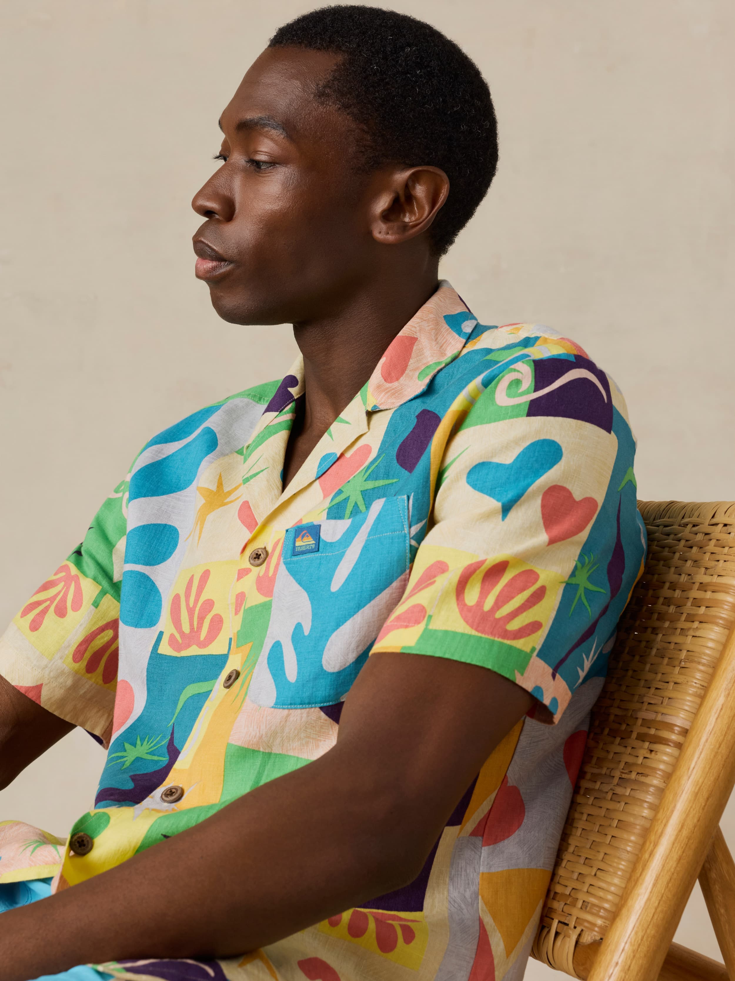 Person wearing a colorful patterned shirt sitting on a chair against a neutral background