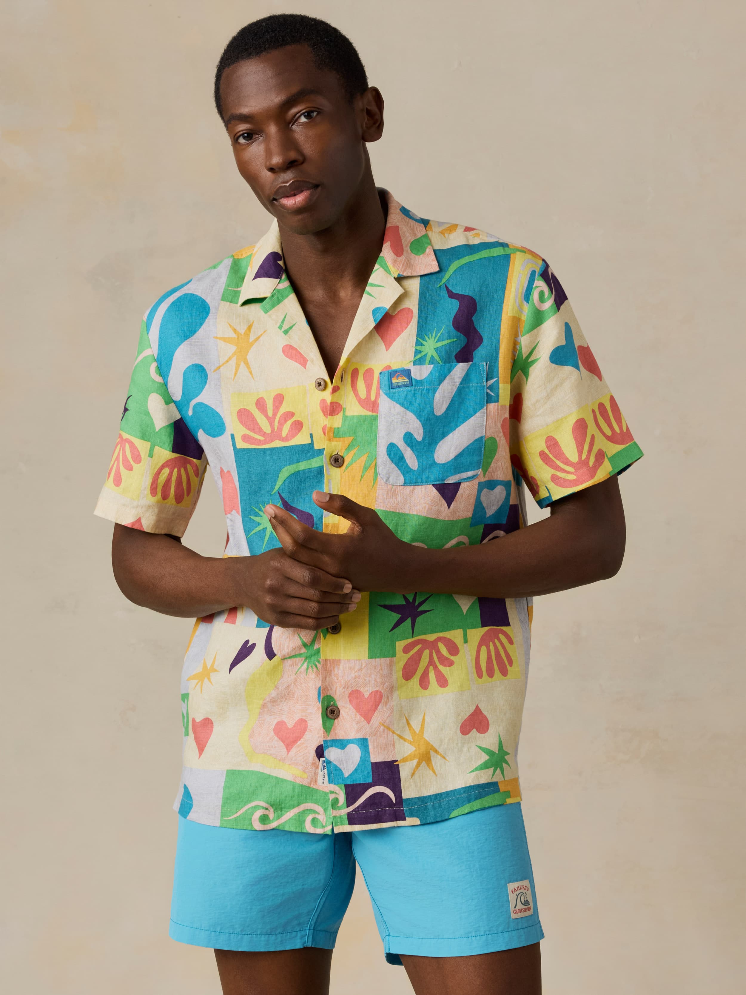 Man wearing a colorful printed shirt and blue swim shorts against a beige background