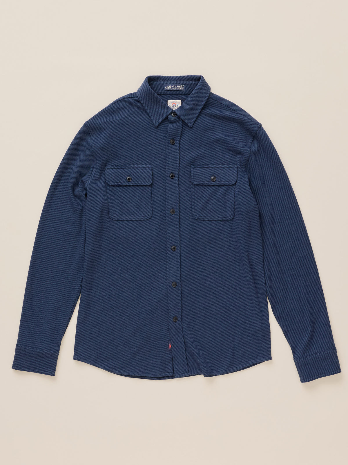 A dark blue long-sleeve button-up shirt with two buttoned chest pockets, laid flat on a light beige background., image 7 of 8