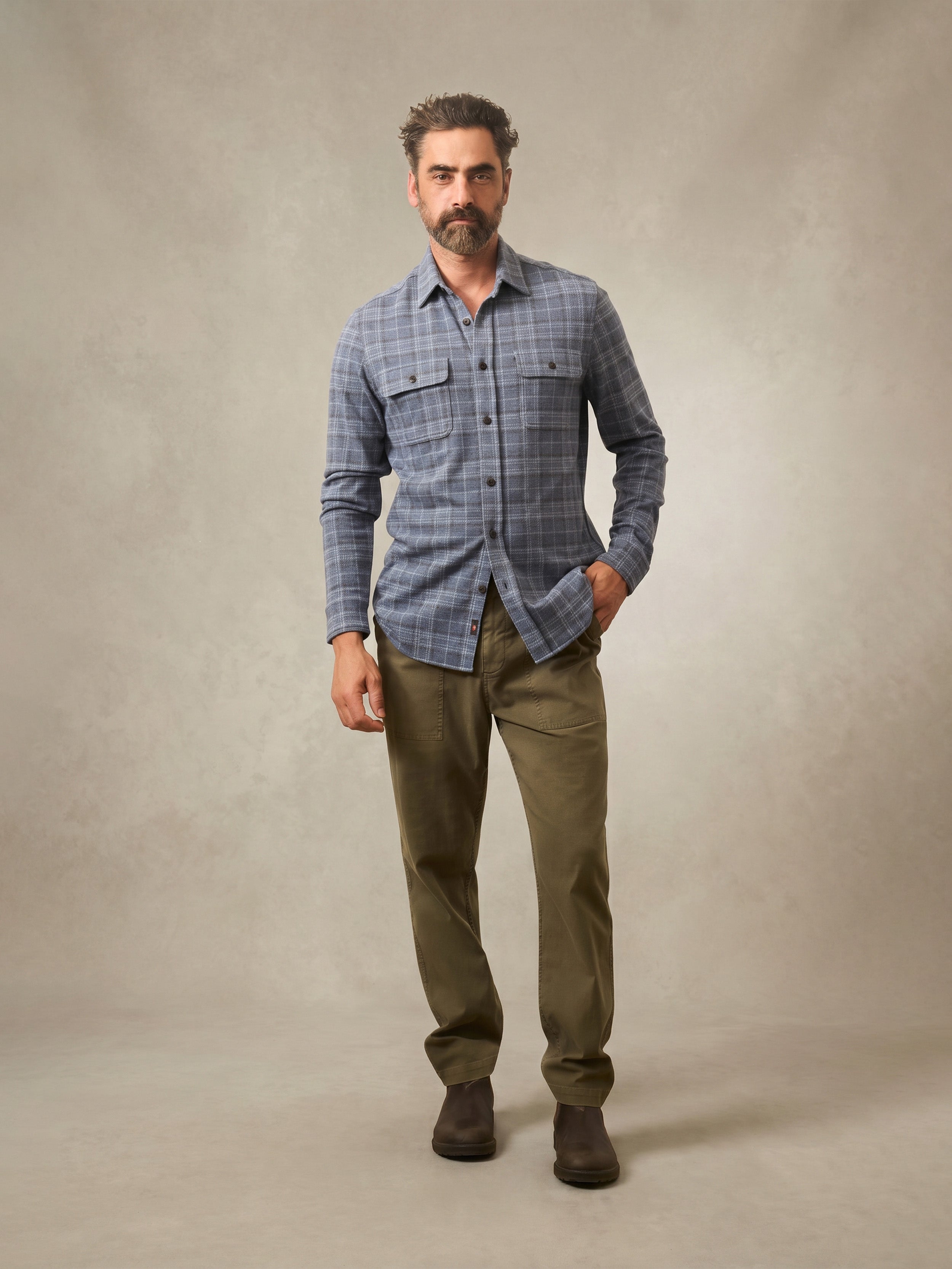Man wearing a blue plaid shirt and green pants against a beige background