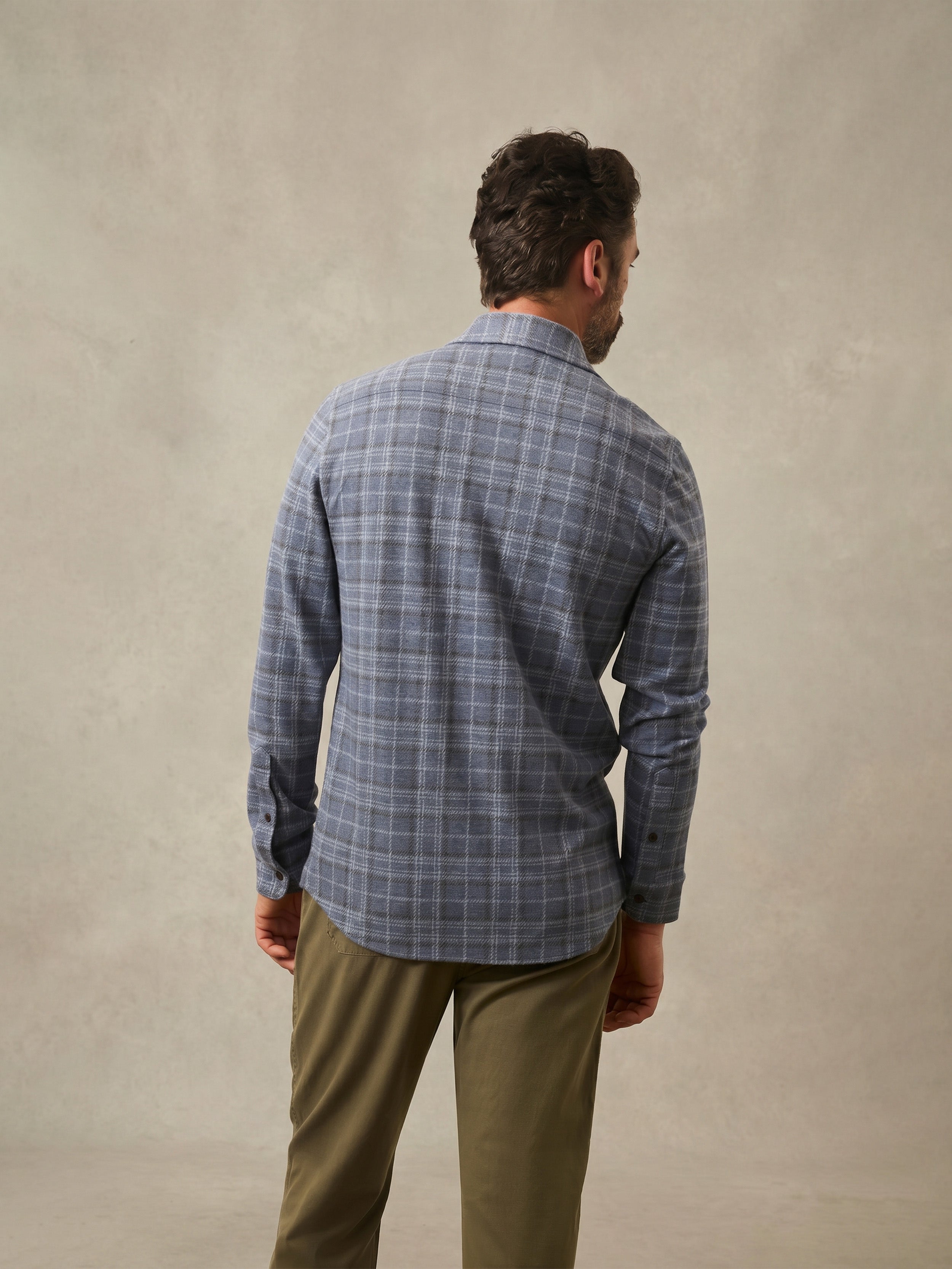 Man wearing a blue plaid shirt and beige pants against a beige background