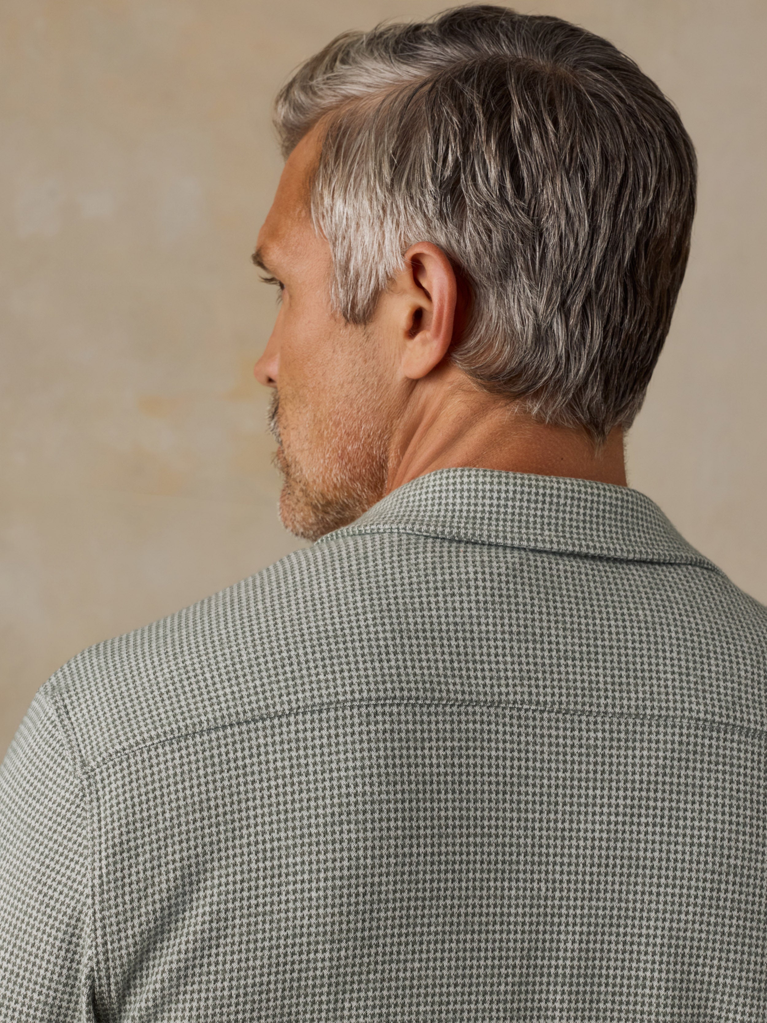 A close-up back view of a man with gray hair wearing a textured, fine-patterned button-down shirt in muted green and white.
