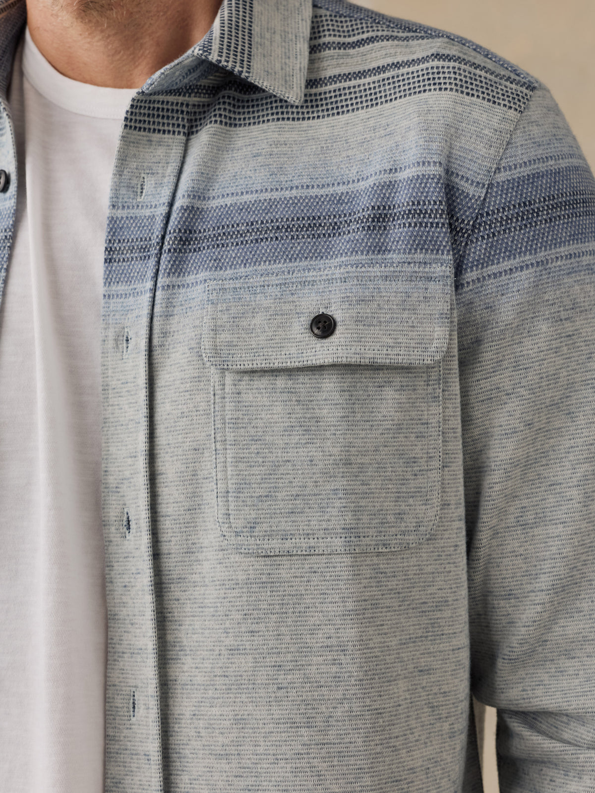 Close-up of a man wearing a light gray and blue striped textured button-down shirt over a white t-shirt., image 7 of 7