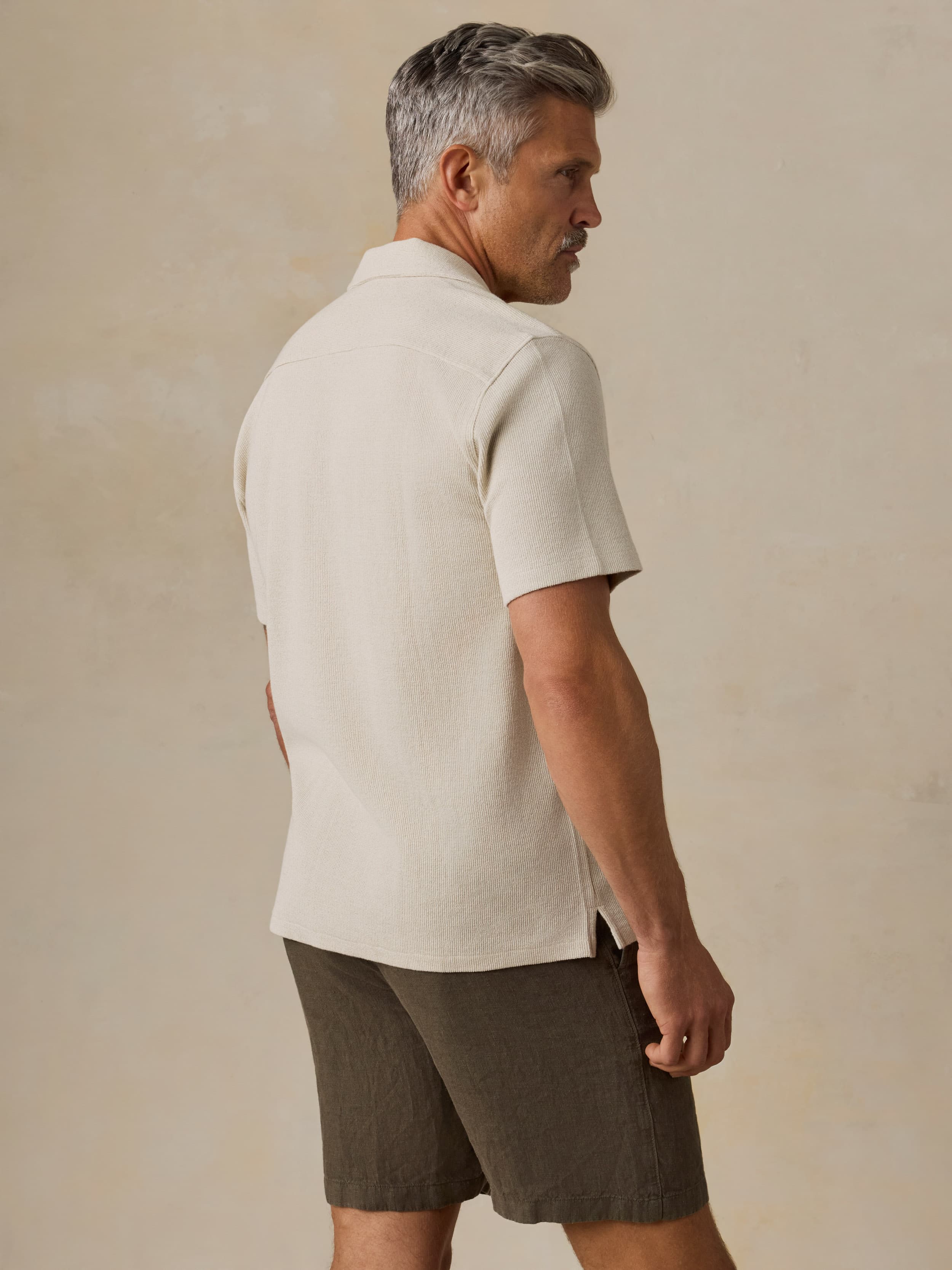 Man wearing a light-colored shirt and brown shorts against a beige background