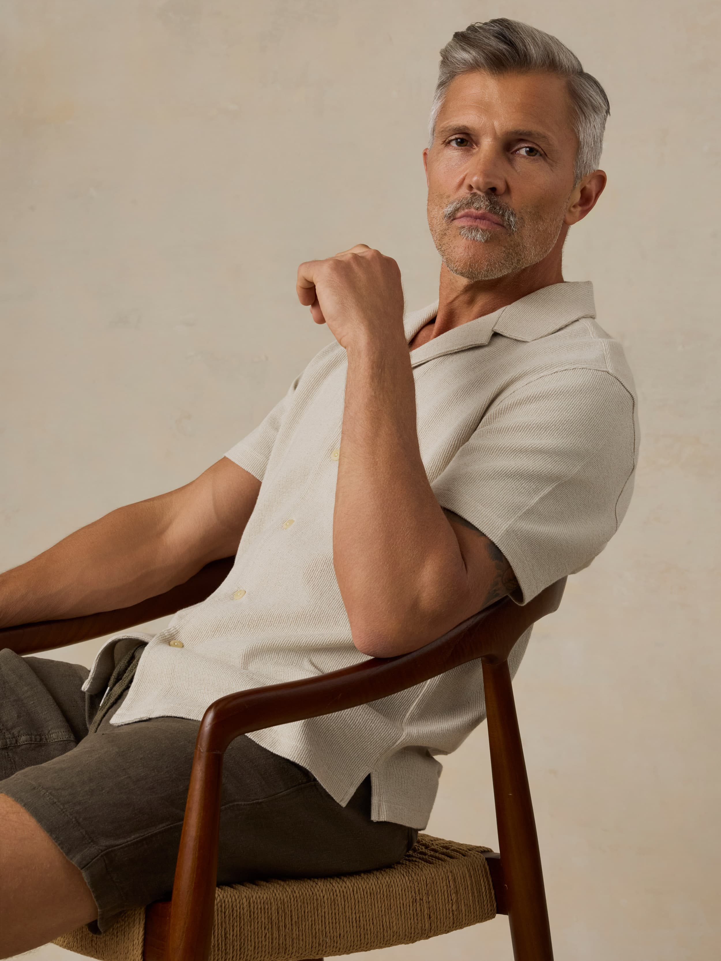 Man sitting on a chair wearing a light-colored shirt against a neutral background