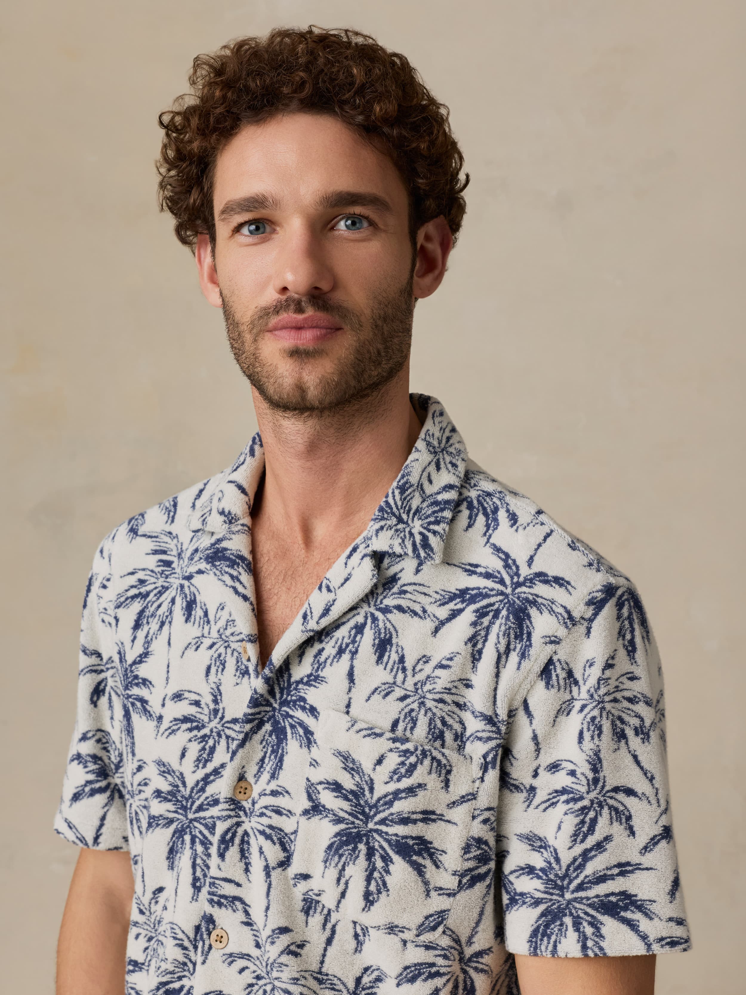 Man wearing a white shirt with blue palm tree pattern against a beige background